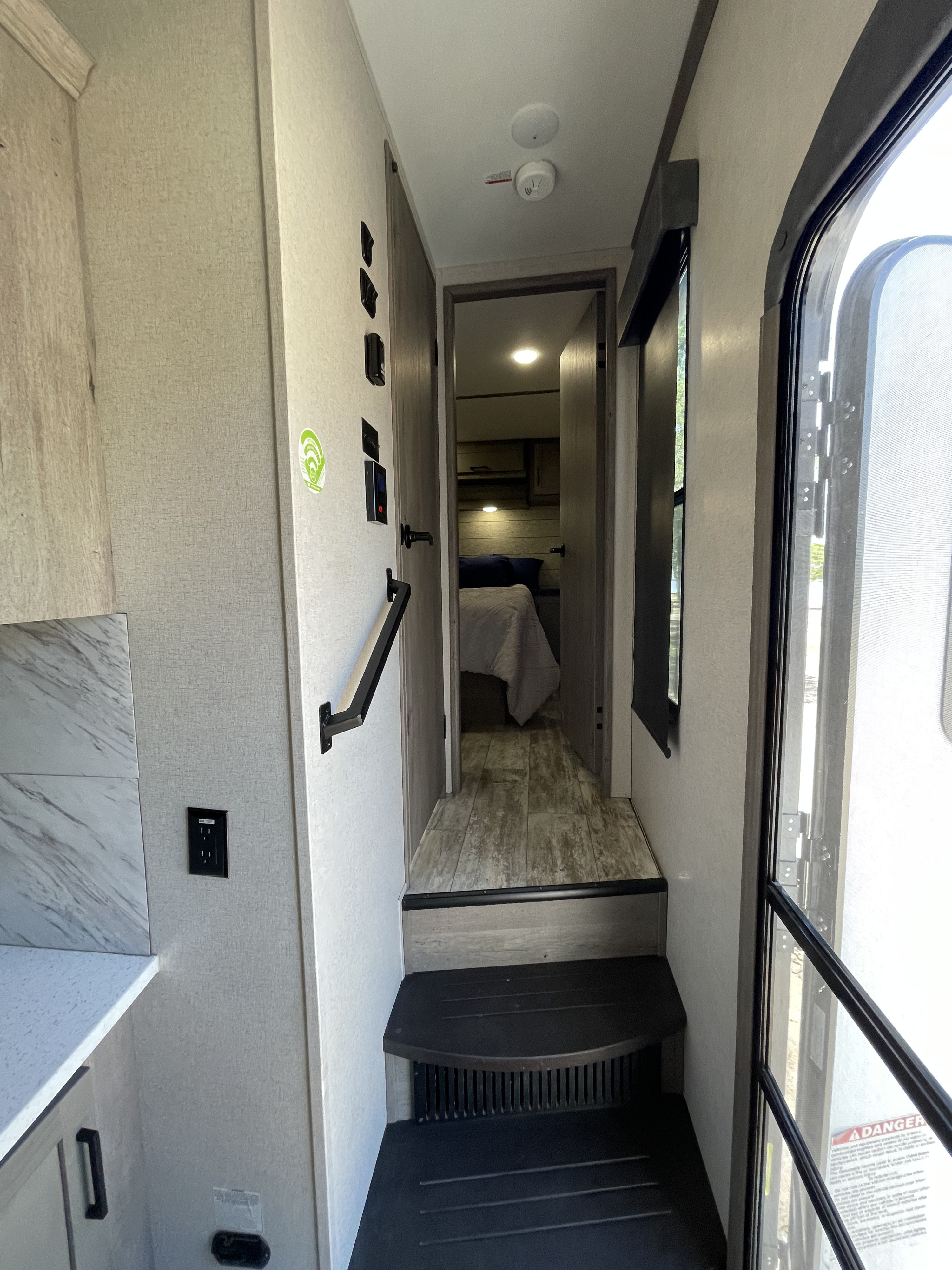This RV rental interior features a functional layout: a hallway to the bedroom, steps to the main area, and controls by the entry.. Keystone Carbon 2021