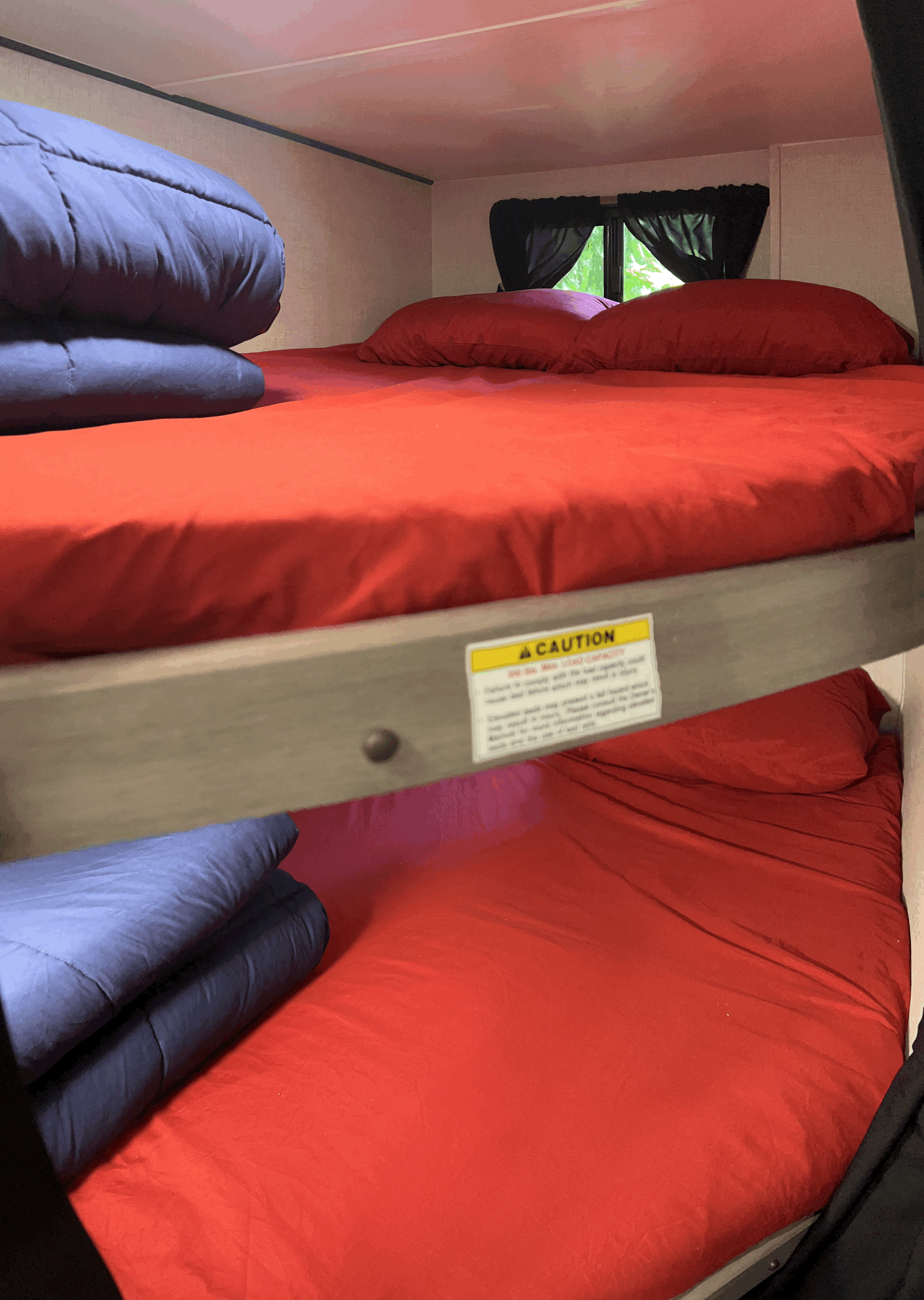 RV rental sleeping area: bunk beds with bright red sheets, blue comforters, and a safety caution label.. Sunset Trail 188BH 2022