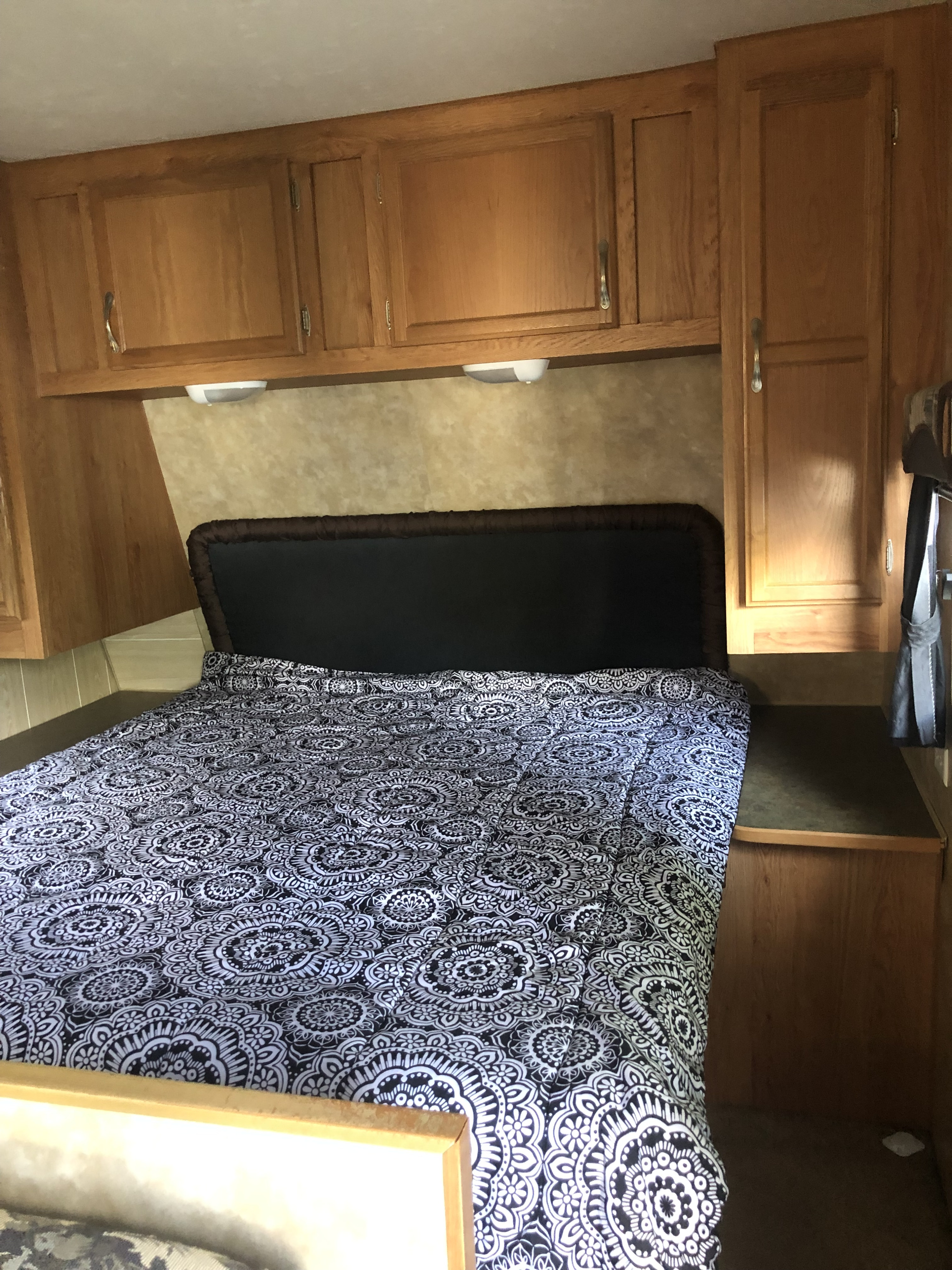 Inside an RV rental: a neatly made bed with a black & white patterned comforter and wooden overhead cabinets.. Jayco Jay Flight 2007