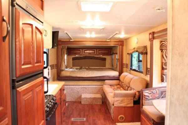 Spacious RV rental interior: kitchen with fridge, living area with sofa, and elevated master bedroom, all with wood accents.. Keystone Outback 250RS 2011