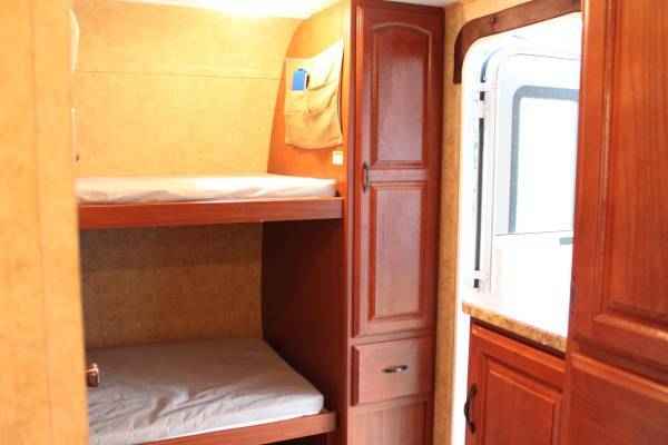 This RV rental offers comfortable bunk beds with white mattresses & wooden storage, great for your camper trip.. Keystone Outback 250RS 2011