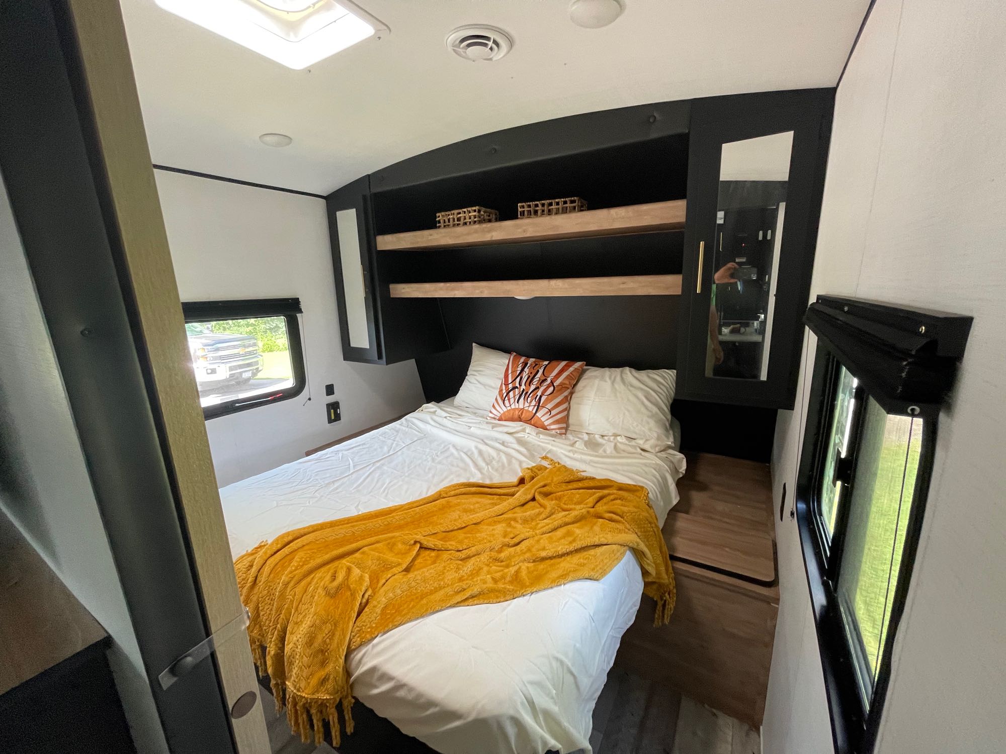 Modern RV rental bedroom featuring a queen bed, cozy yellow throw, and smart overhead storage.. Keystone RV Springdale 2023