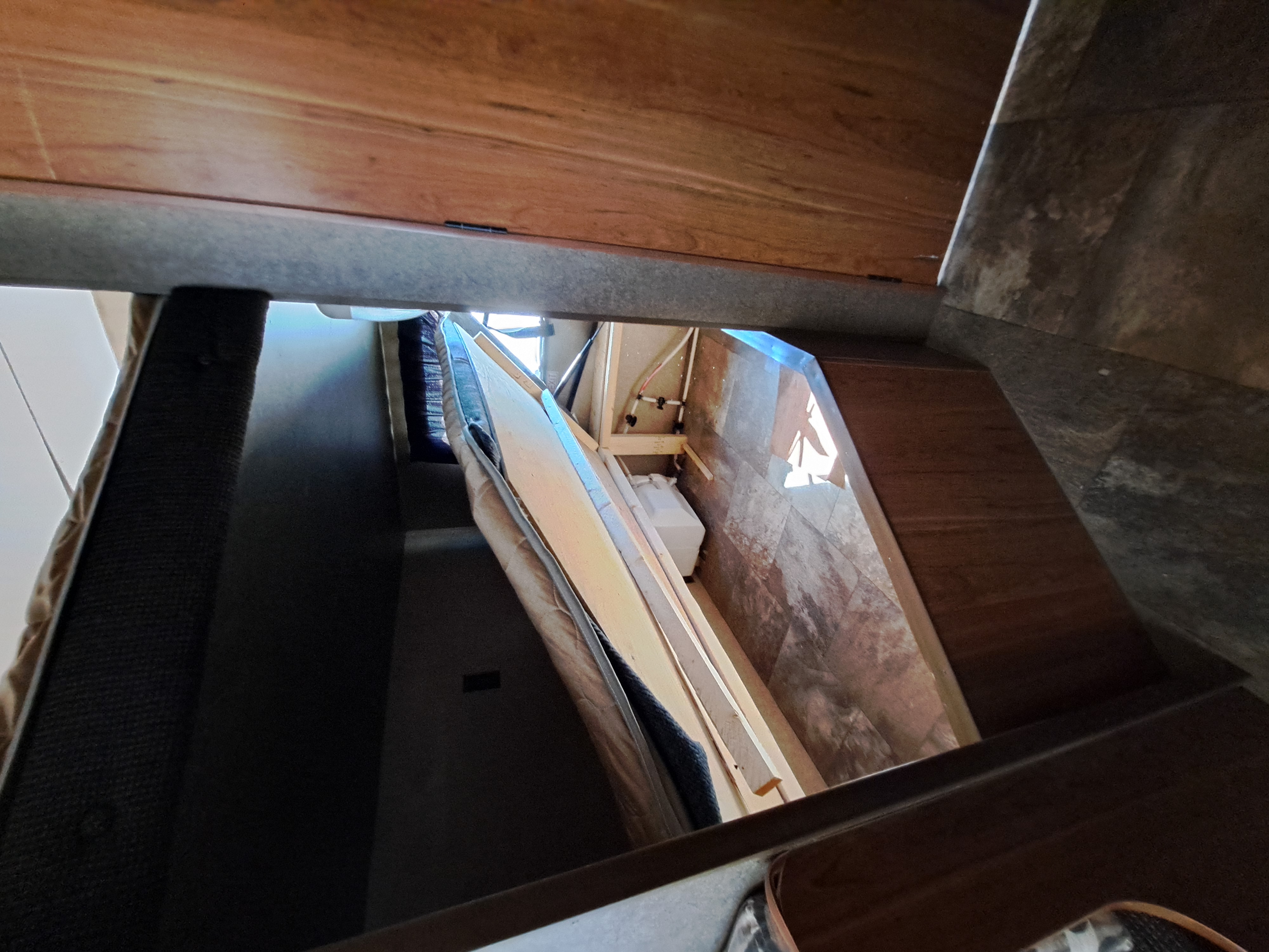 Under-bed storage of an RV rental, showing lifted mattress, wooden supports, and hidden plumbing.. Starcraft AR-One Maxx 2015