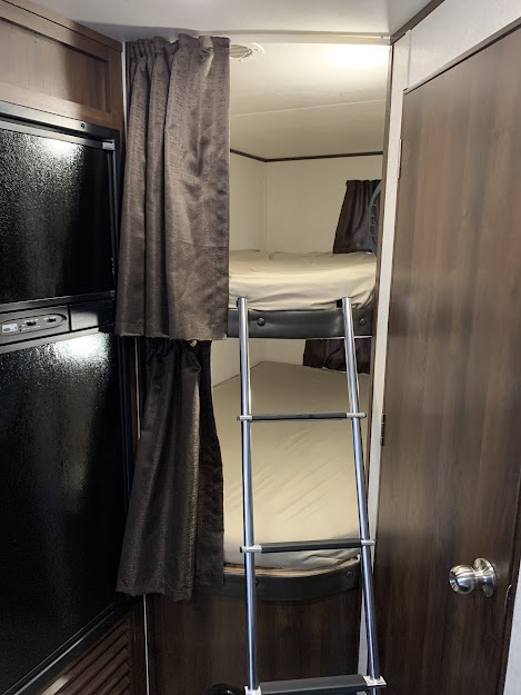 RV rental interior: bunk beds with ladder, privacy curtains, and a black built-in refrigerator.. Jayco Jay Flight SLX 2019