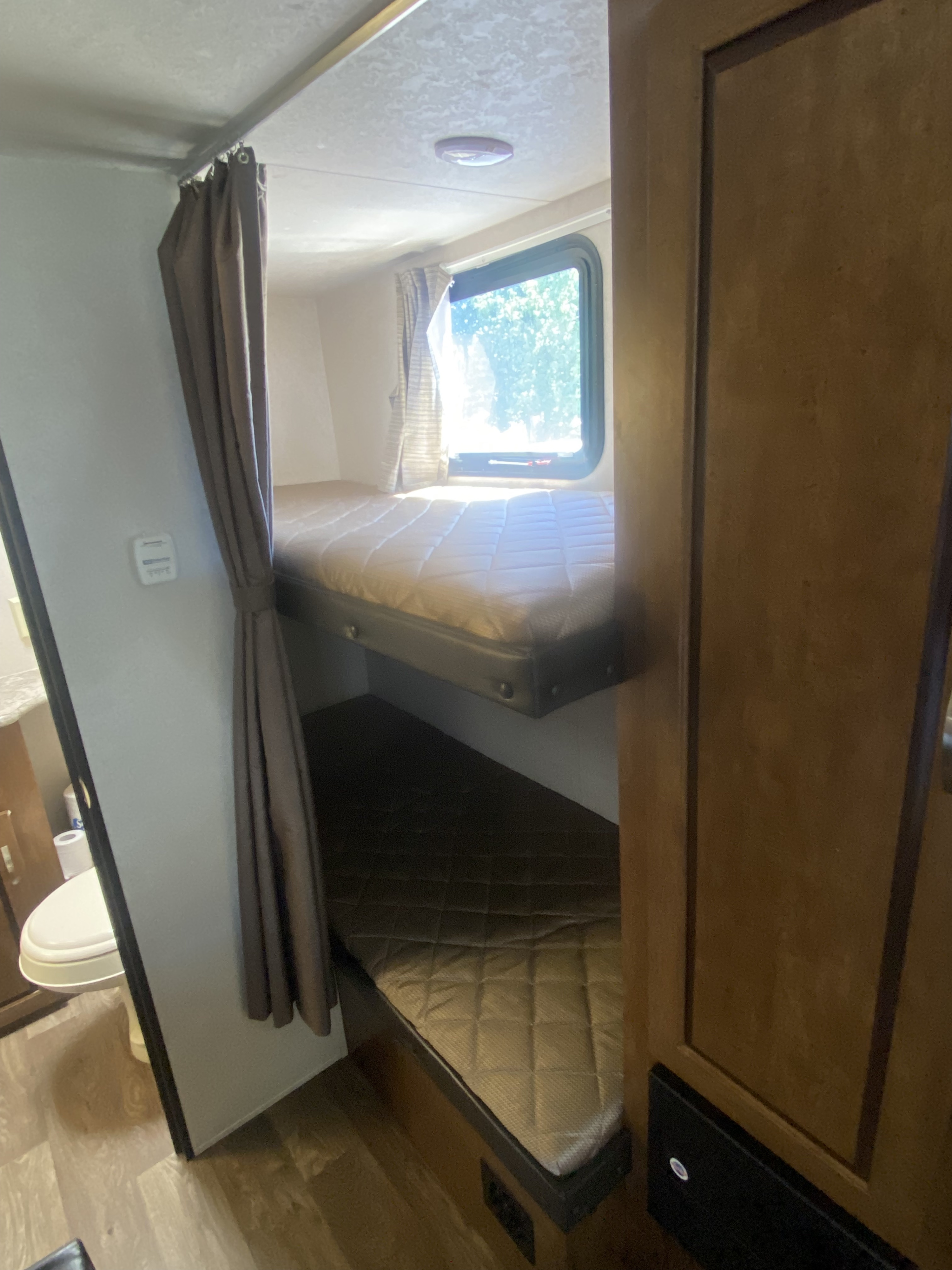 RV rental interior: practical bunk beds with privacy curtain, ceiling light, and a compact bathroom beyond.. Forest River Salem Cruise Lite 2018