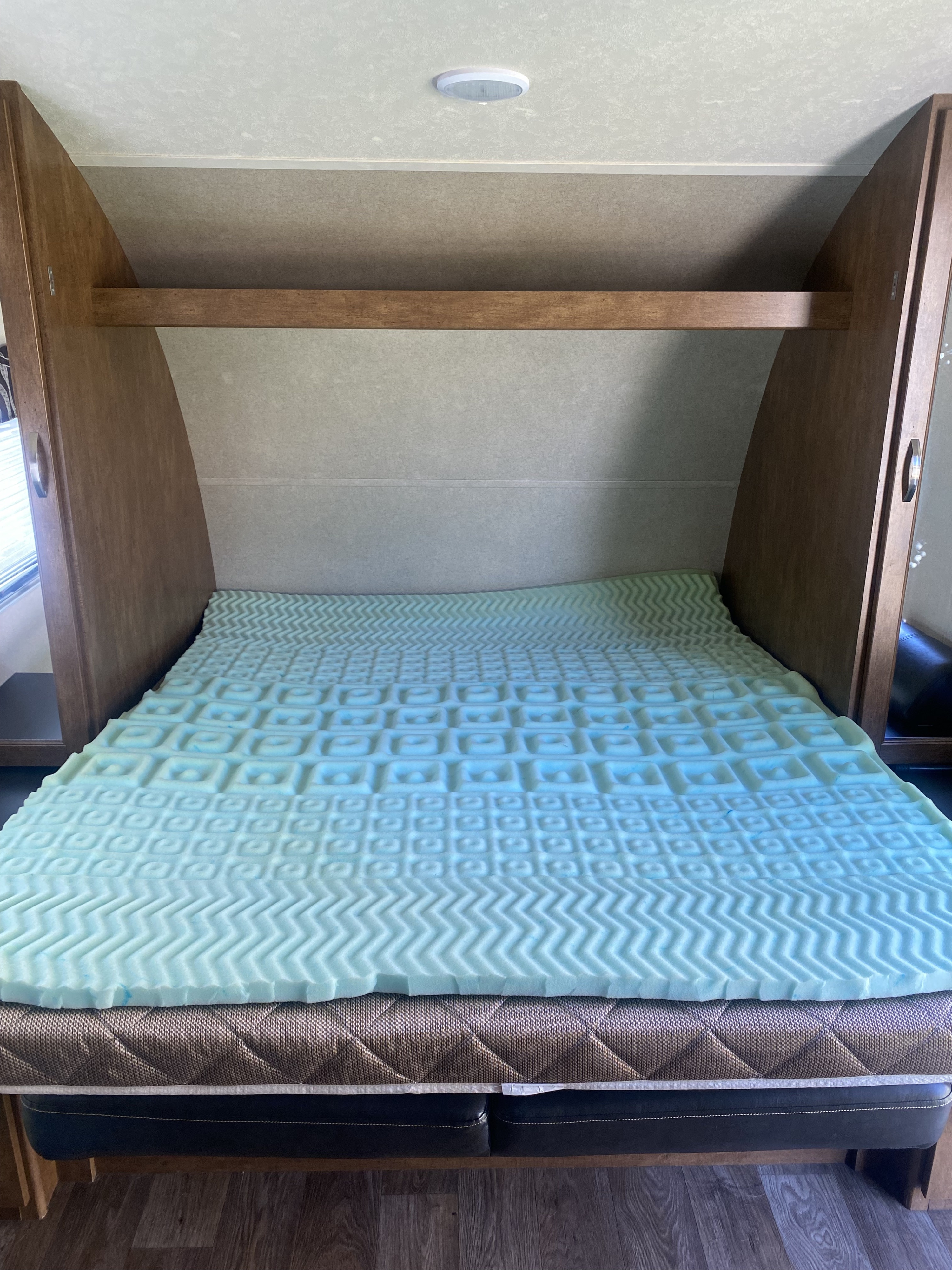 An RV rental bedroom featuring a bed with a light blue, textured foam mattress topper and wooden shelving.. Forest River Salem Cruise Lite 2018