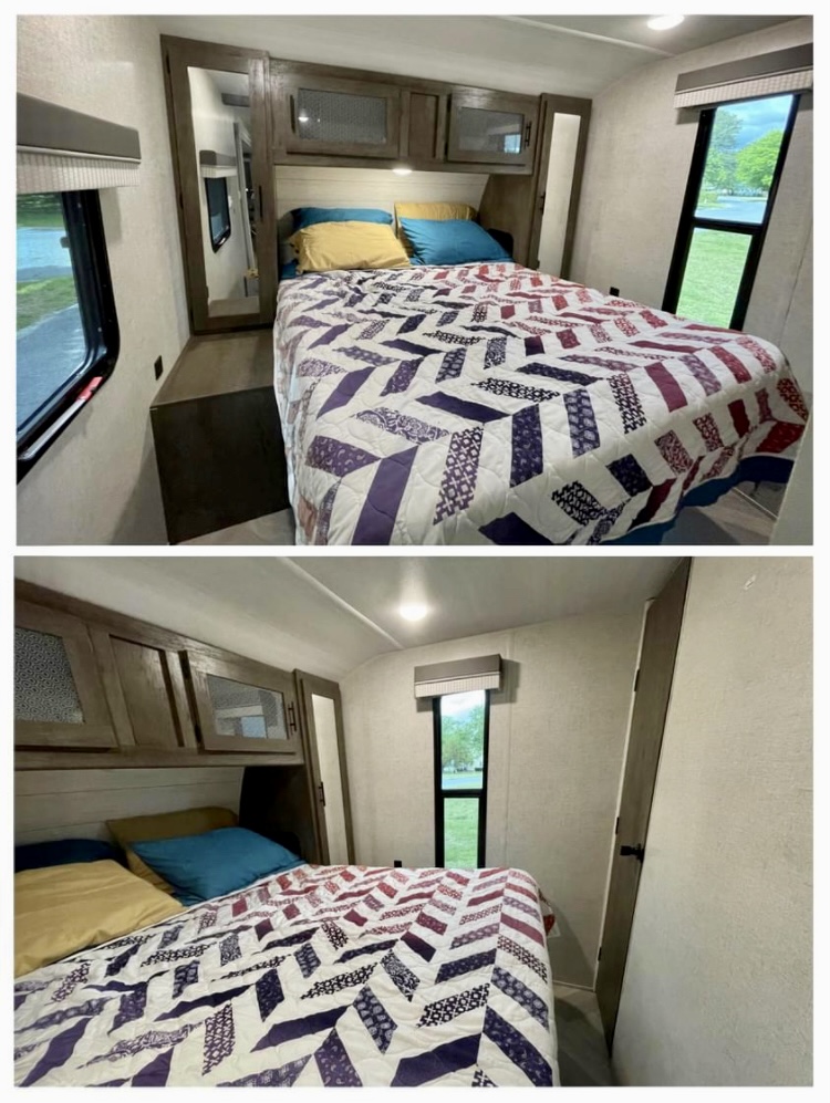Inside a cozy RV rental: This bedroom features a patterned quilt, overhead cabinets, and a window offering a scenic view.. Forest River Wildwood 2021