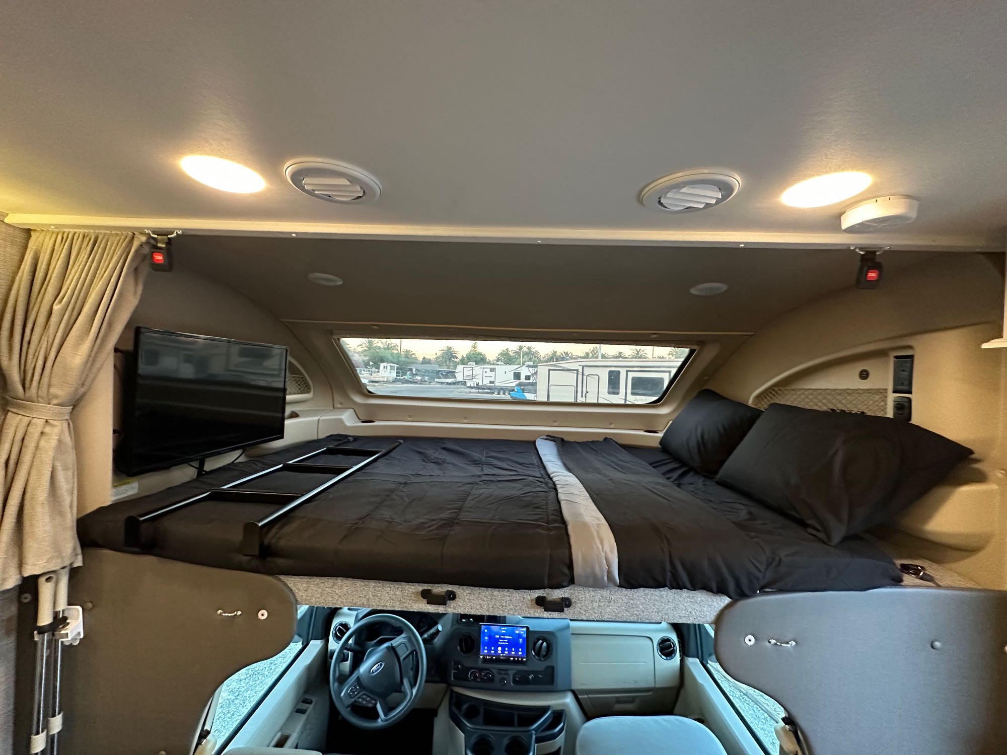 An rv rental's interior, featuring a cab-over bed with TV and ladder, plus the driver's cockpit below.. Entegra Coach Odyssey 2022