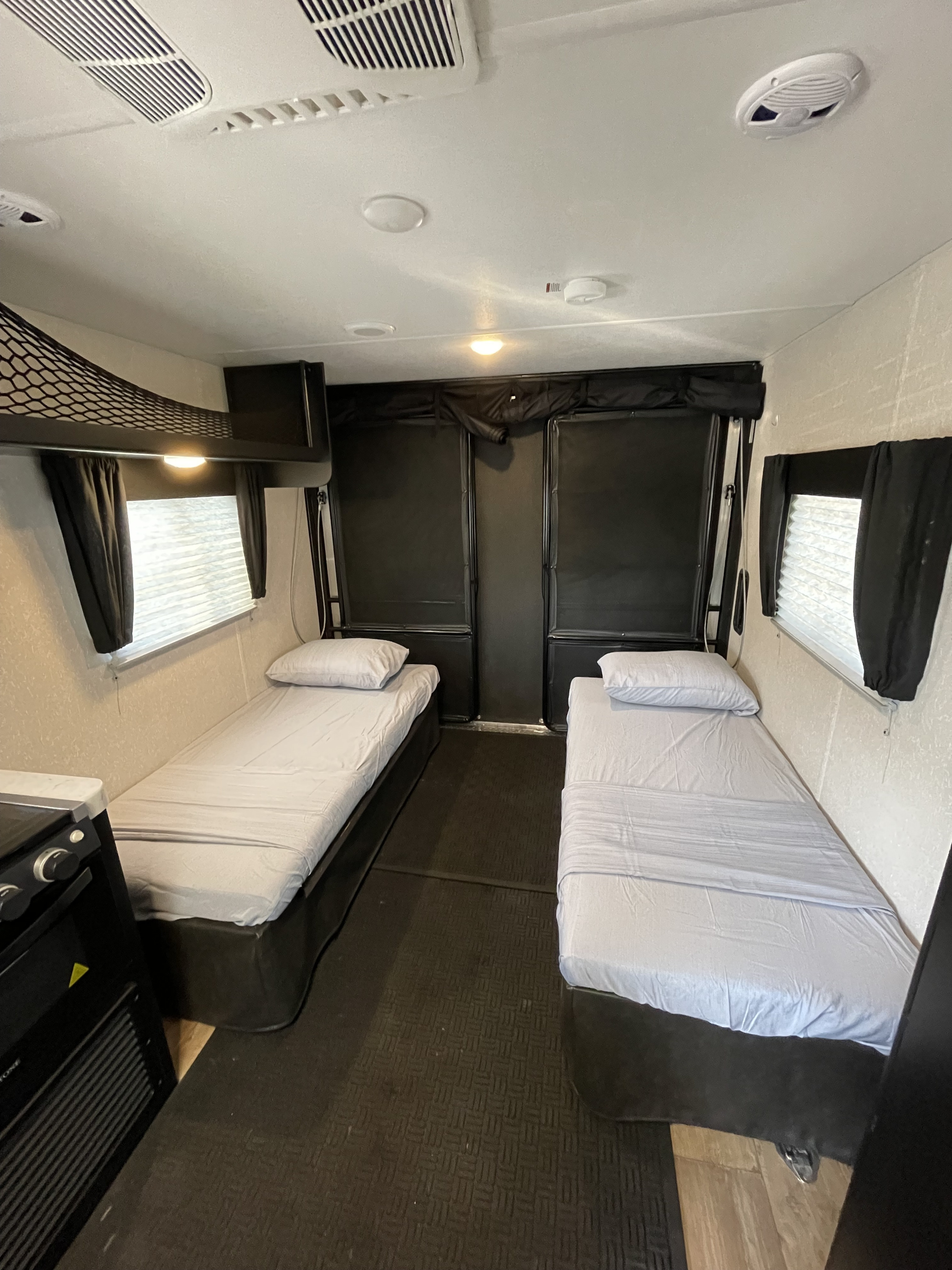 RV rental interior featuring two twin beds with light sheets, a small kitchen counter, and textured walls. Ceiling vents and lights visible.. Forest River Wolf Pup 2021