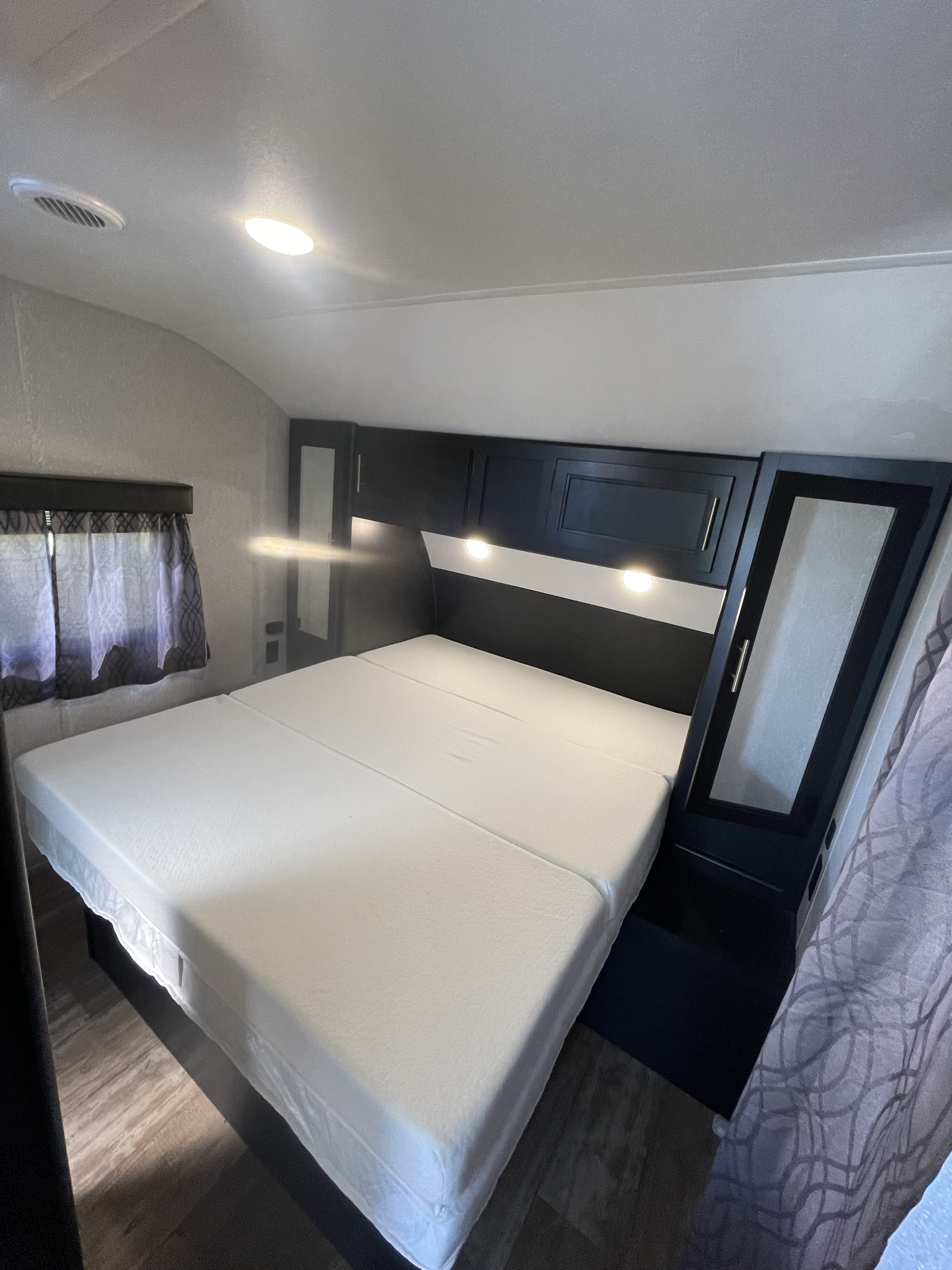 RV rental bedroom interior: a comfortable bed with overhead cabinets, task lighting, and patterned curtains.. Forest River Wolf Pup 2021