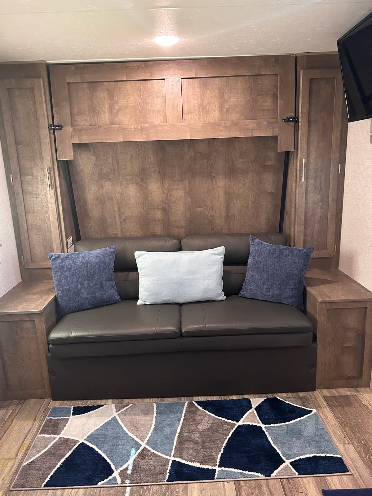 Cozy RV rental interior: dark sofa with blue pillows, wood paneling, storage cabinets, and a modern geometric rug.. KZ Escape 2020