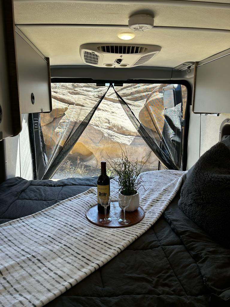 Cozy RV rental bedroom with a comfy bed, wine, and a beautiful desert view through screened doors. Ideal for travel.. Winnebago Solis 2023