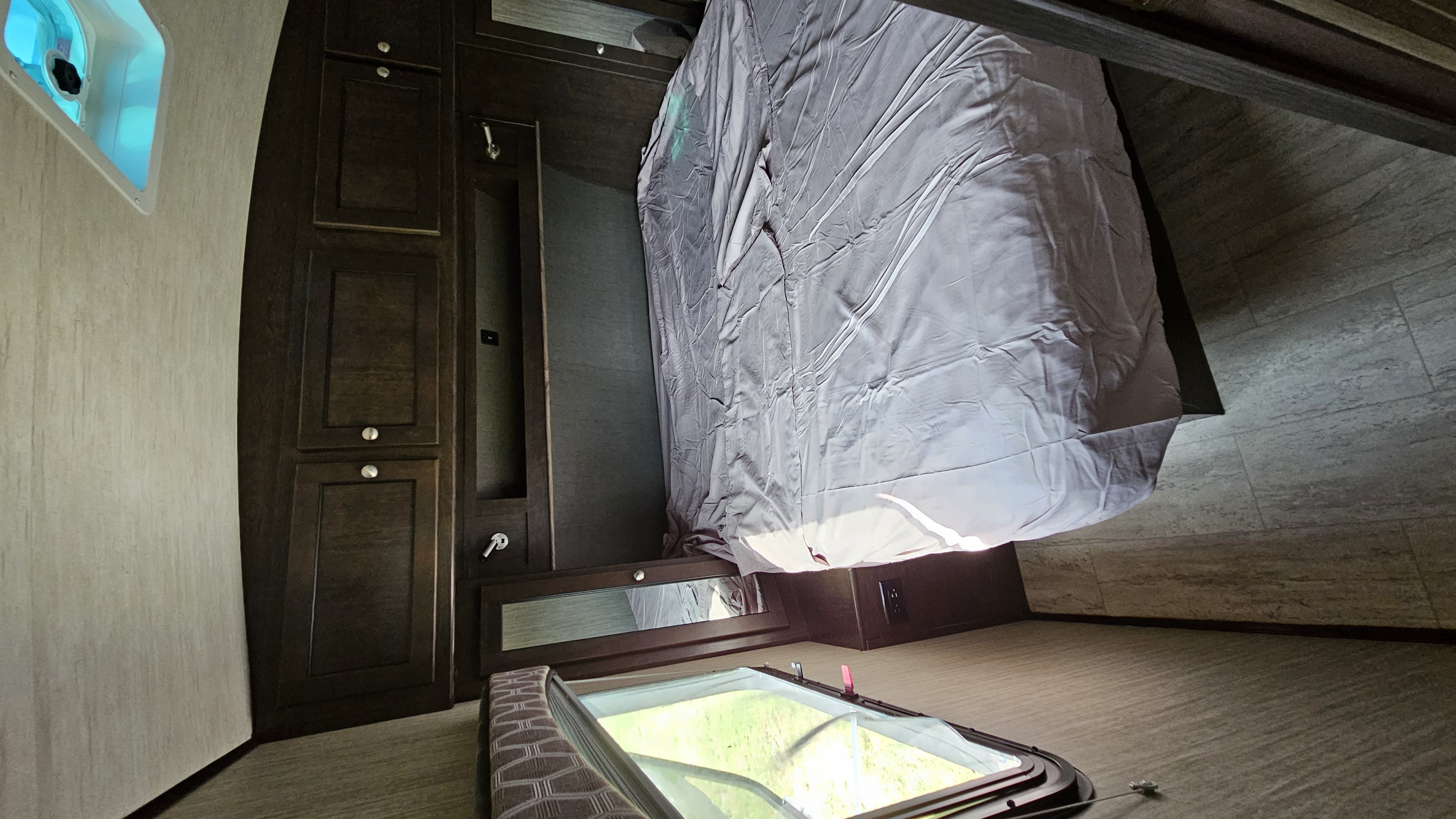 Cozy RV rental bedroom featuring a made bed, dark wood built-in storage, and unique floor-level window.. Cruiser RV Shadow Cruiser 2019