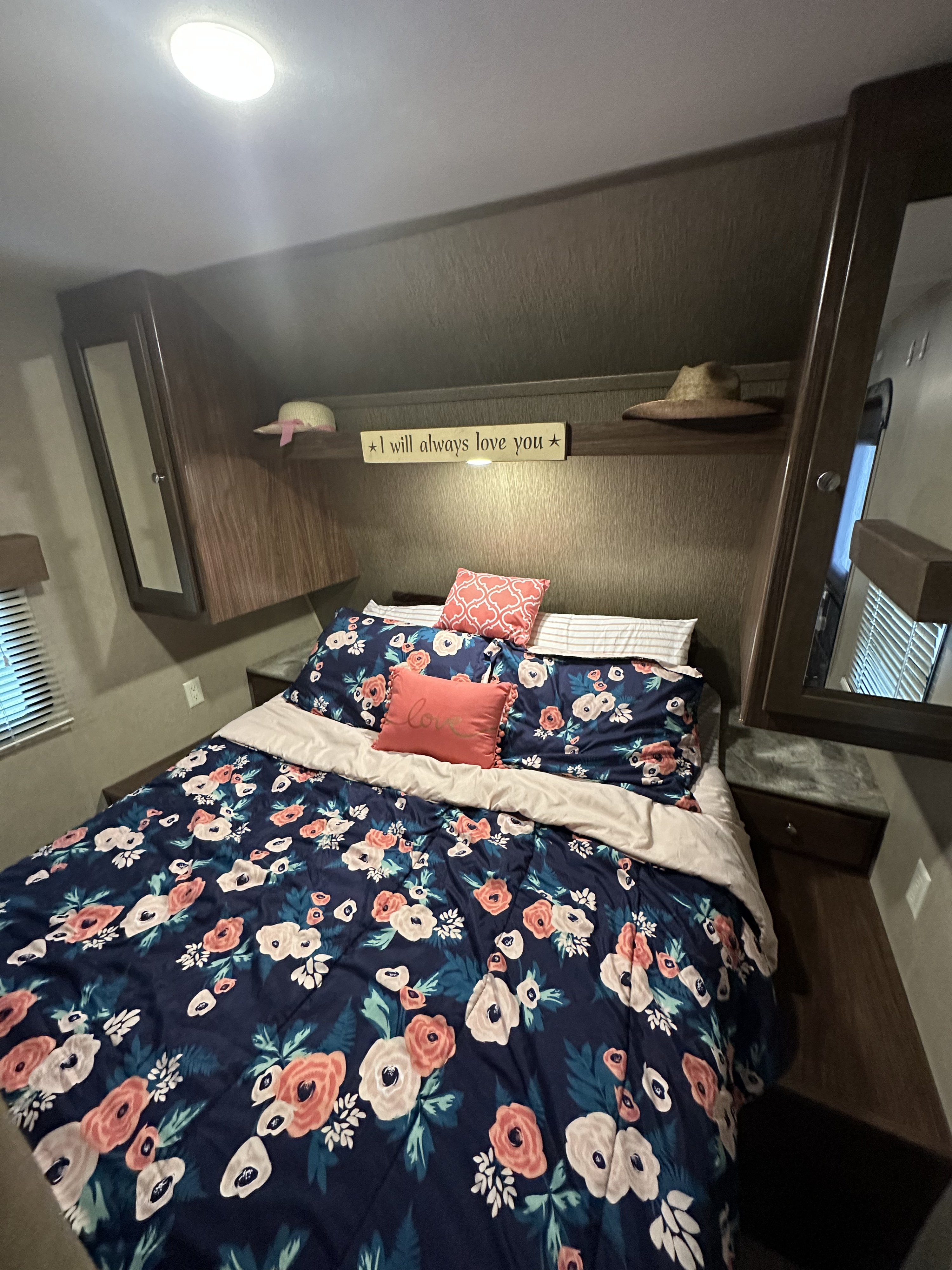 A cozy RV rental bedroom featuring a bed with navy floral bedding, decorative pillows, and overhead storage.. Coachmen 264bh 2017