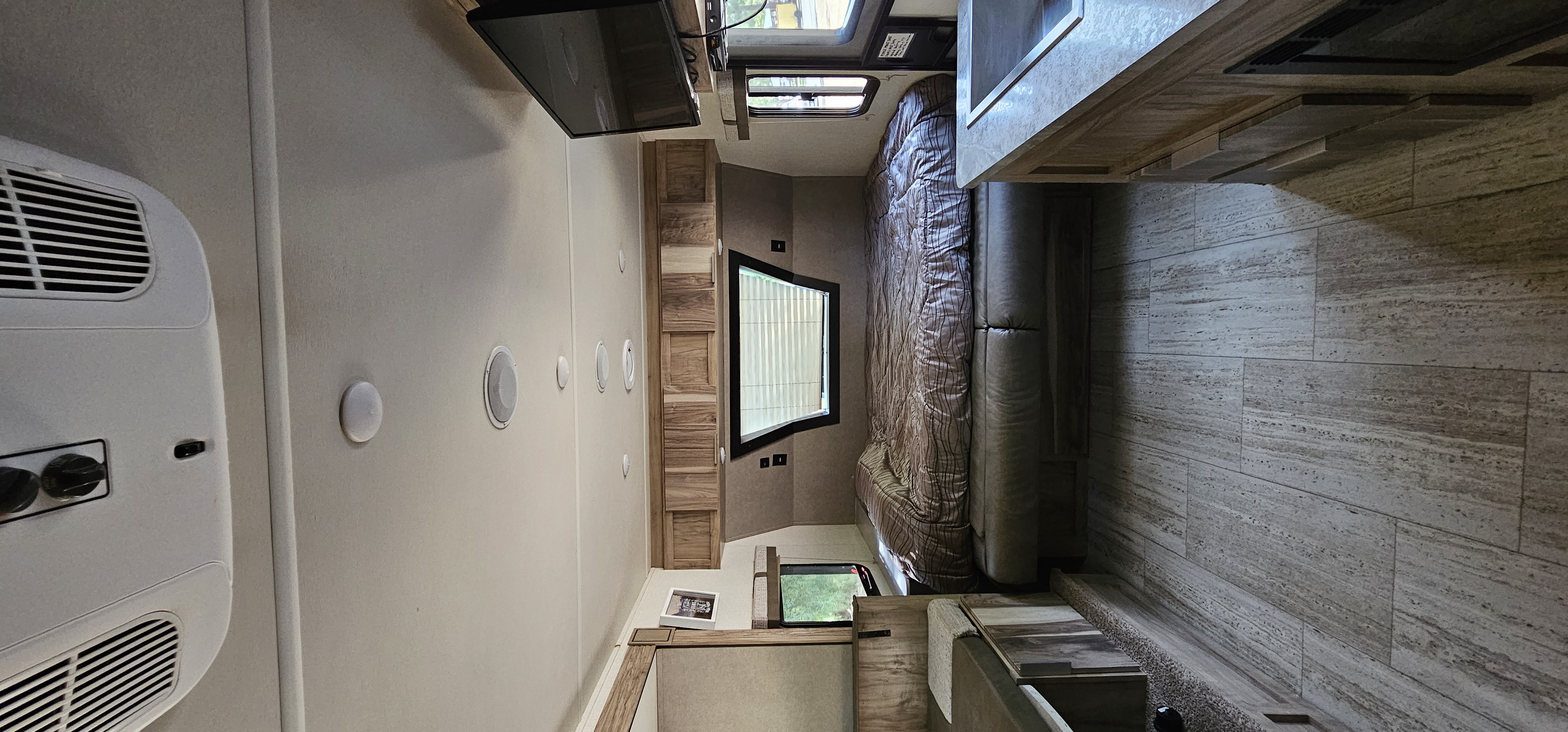 Modern RV rental interior: bedroom with bed, TV, AC unit, and tiled flooring extending to kitchen. Compact living space.. Forest River Palomino Real-Lite Mini 2021