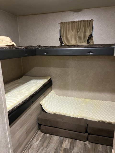 Inside an RV rental: L-shaped upper bunks and two lower foam-topped beds with a window.. Forest River Coachmen Catalina Legacy 2019