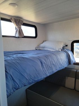 **RV rental** bunk bed interior: A cozy sleeping space with blue bedding, windows, and a sofa below.. Forest River Wildwood X-Lite 2022
