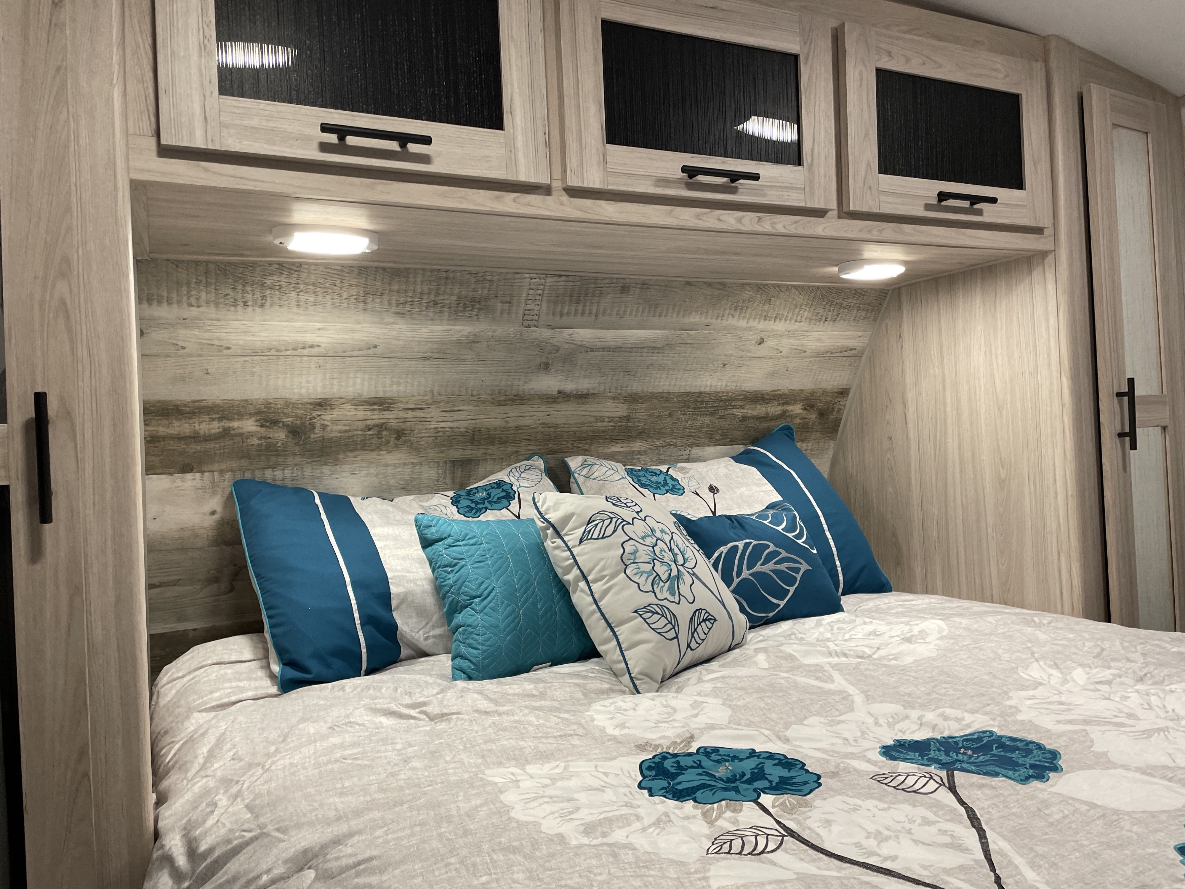 Cozy RV rental bedroom featuring blue & white floral bedding, overhead cabinets, and light wood interior.. Heartland RVs Sundance Ultra Lite 2022