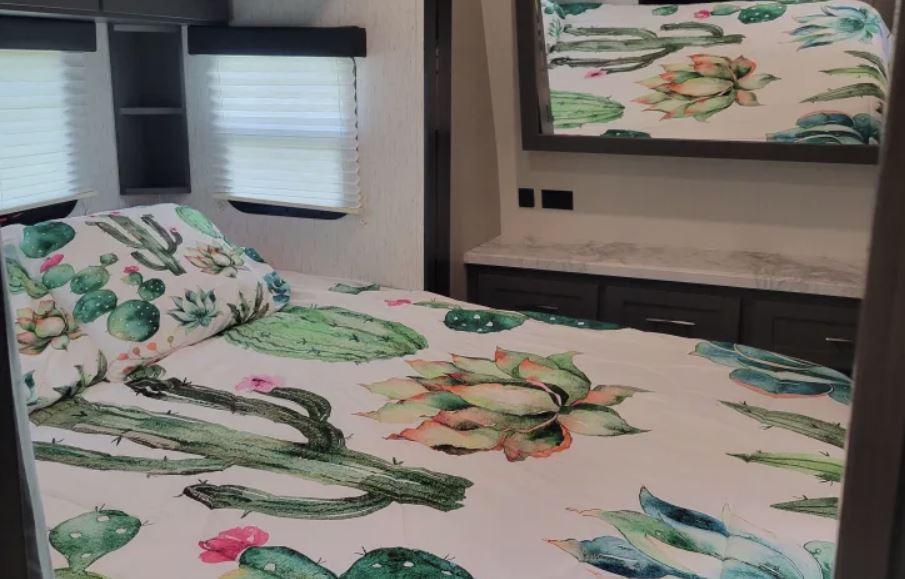 Cozy RV rental bedroom with a vibrant cactus-themed bed and built-in storage. Ideal for your next journey.. Grand Design Momentum 2022