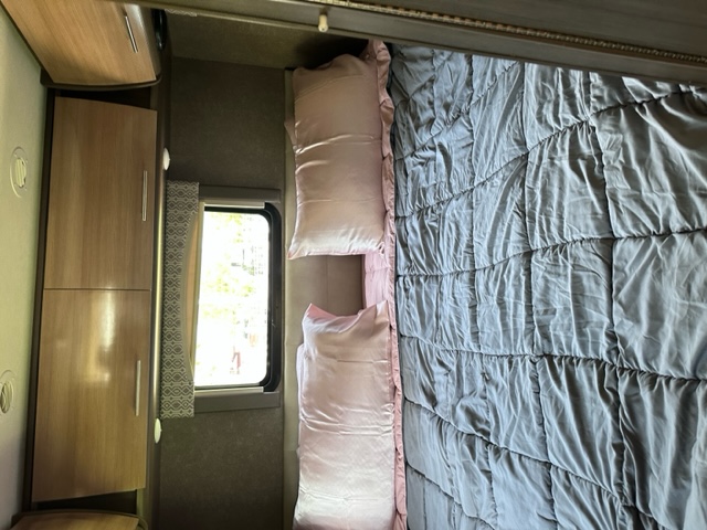 Cozy RV rental bedroom with gray comforter, pink pillows, a bright window, and light wood cabinets.. Thor Vegas 2018