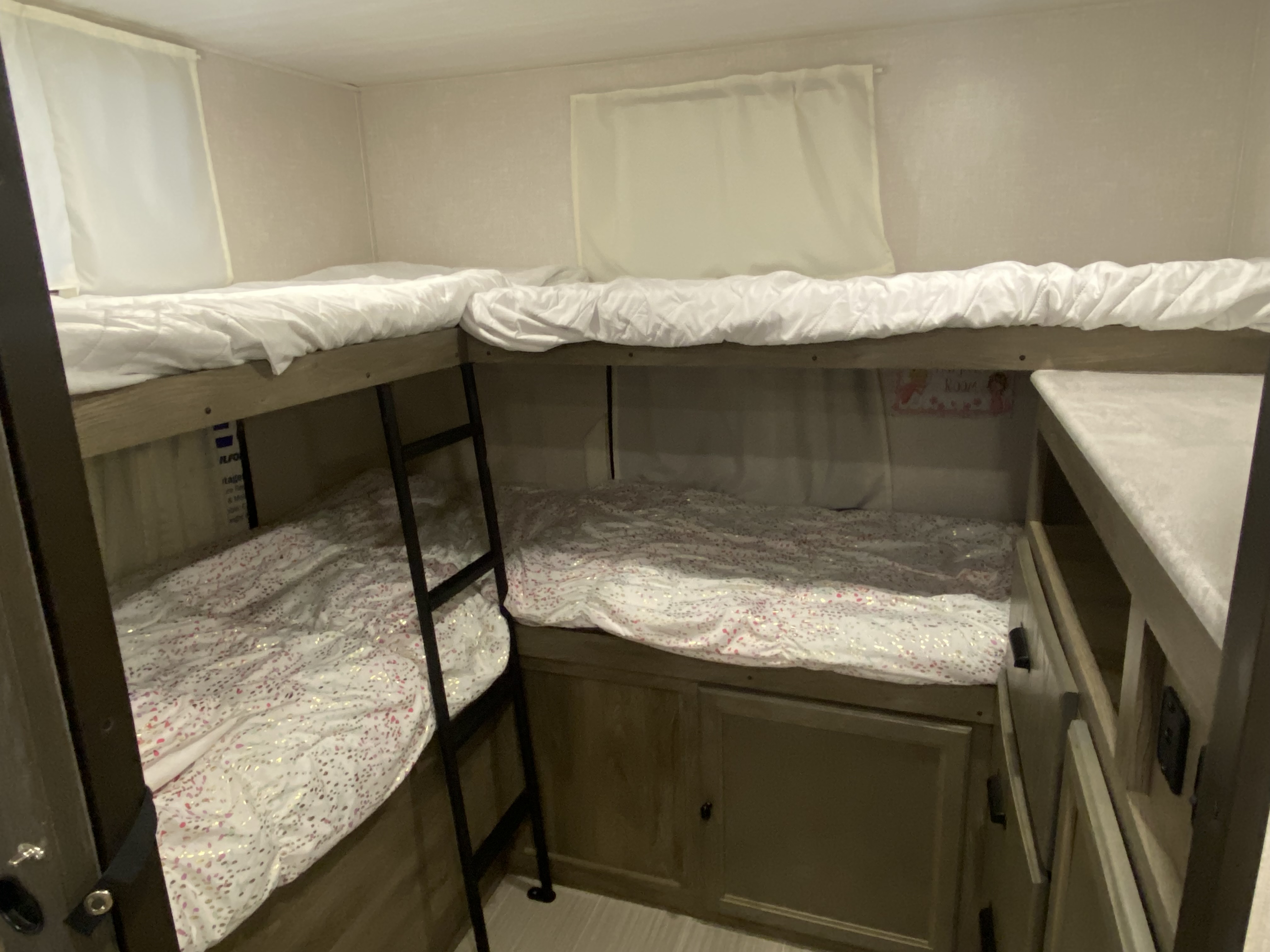 Inside an RV rental: cozy bunk beds with white and patterned bedding, a ladder, and integrated storage, perfect for kids.. Forest River Surveyor 2021
