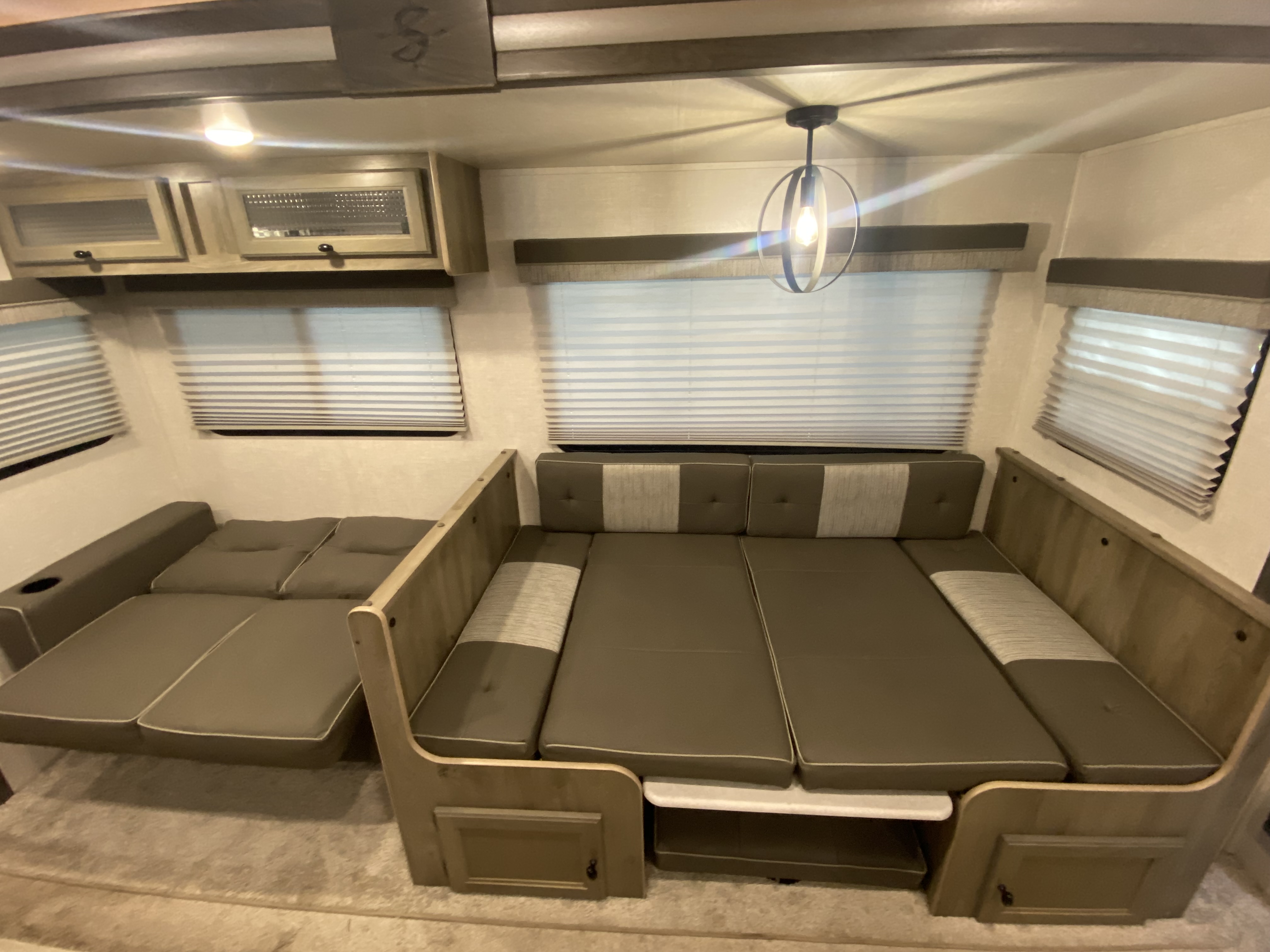 This RV rental interior shows a versatile U-shaped dinette and lounge, both convertible to beds. Features storage, blinds, and modern lighting.. Forest River Surveyor 2021