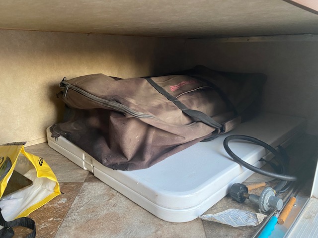 RV rental under-storage: a canvas gear bag, white foldable table, and propane hose for outdoor cooking.. Crossroads RV Zinger 2014