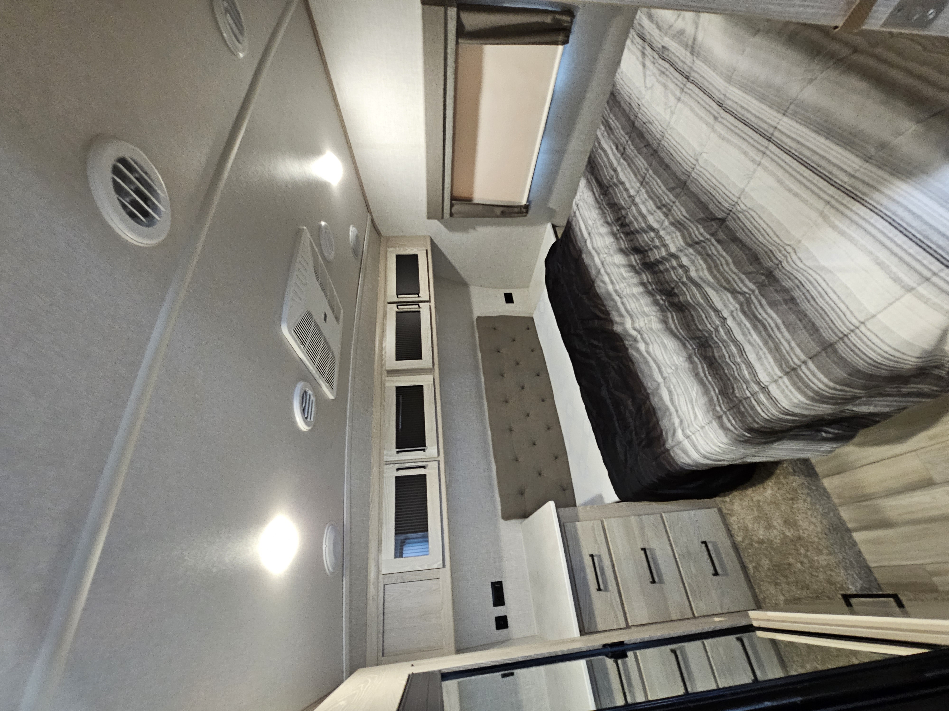 Inside a modern RV rental: a cozy bedroom with striped bedding, cabinet storage, and ceiling AC vents.. Forest River Flagstaff Super Lite 2022