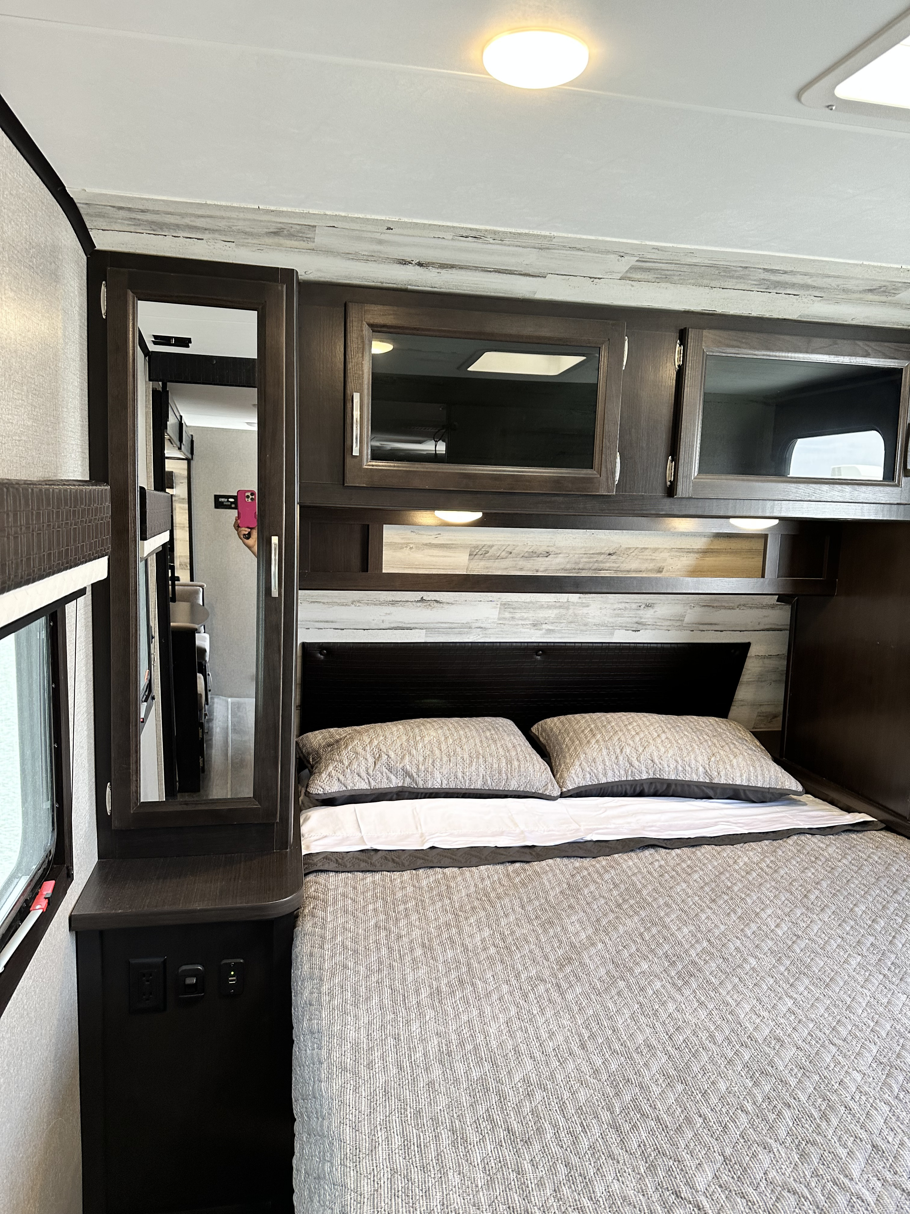 Cozy RV rental bedroom with a quilted comforter, wood-paneled wall, dark cabinets, and a mirror reflecting the RV interior.. Jayco Jay Feather 2021