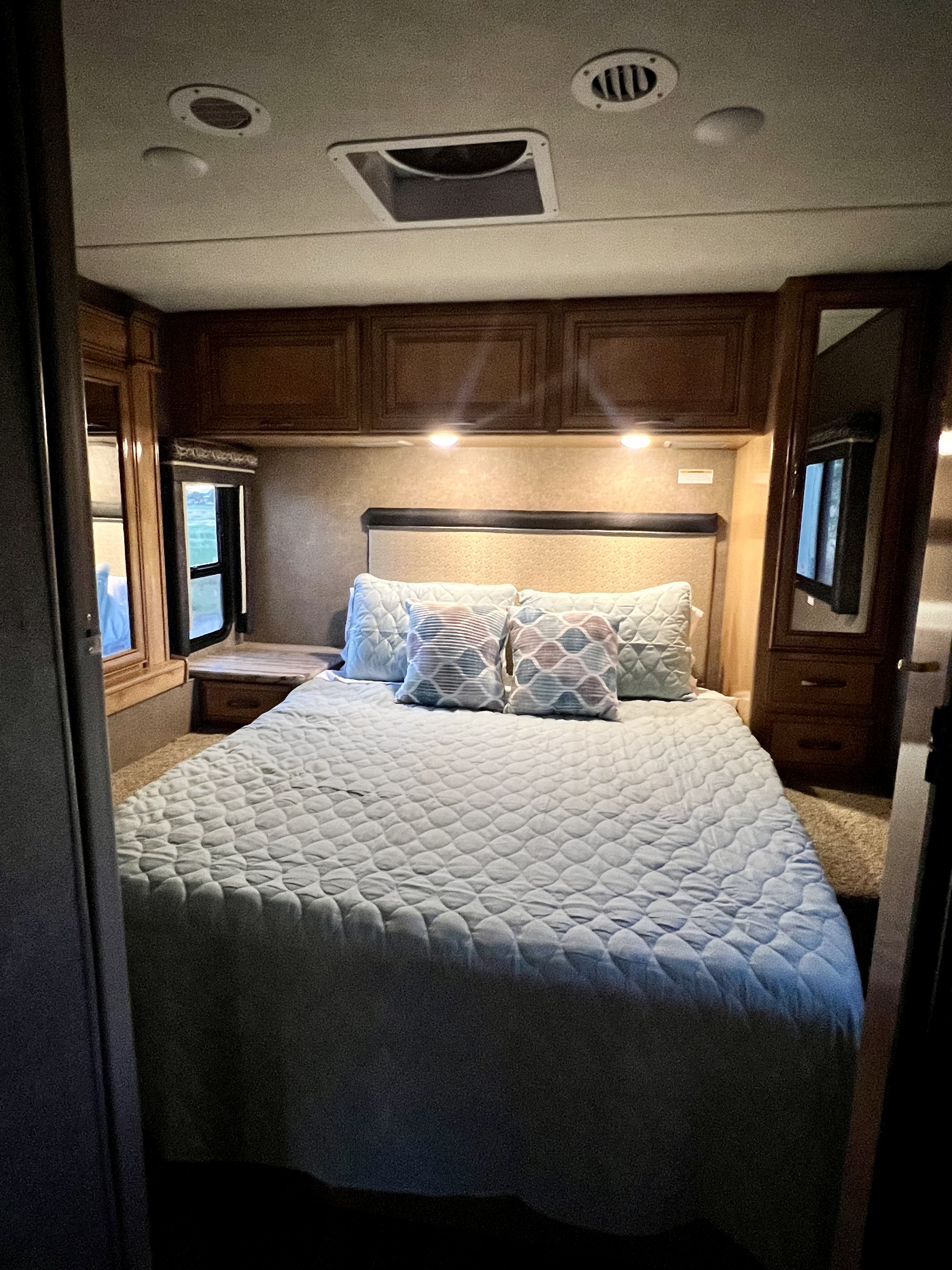 Interior view of a cozy RV rental bedroom featuring a quilted bed, built-in storage, and windows.. Thor Quantum 2018