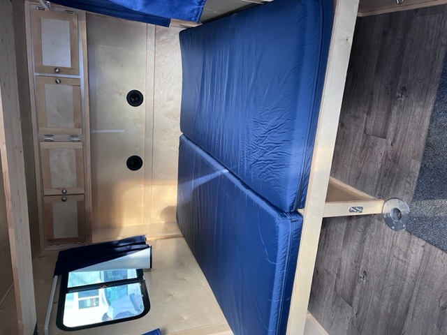 Inside a compact rv rental: two blue bunk beds on the right, light wood cabinets on the left, and a window below.. Escapade Alpine 2018