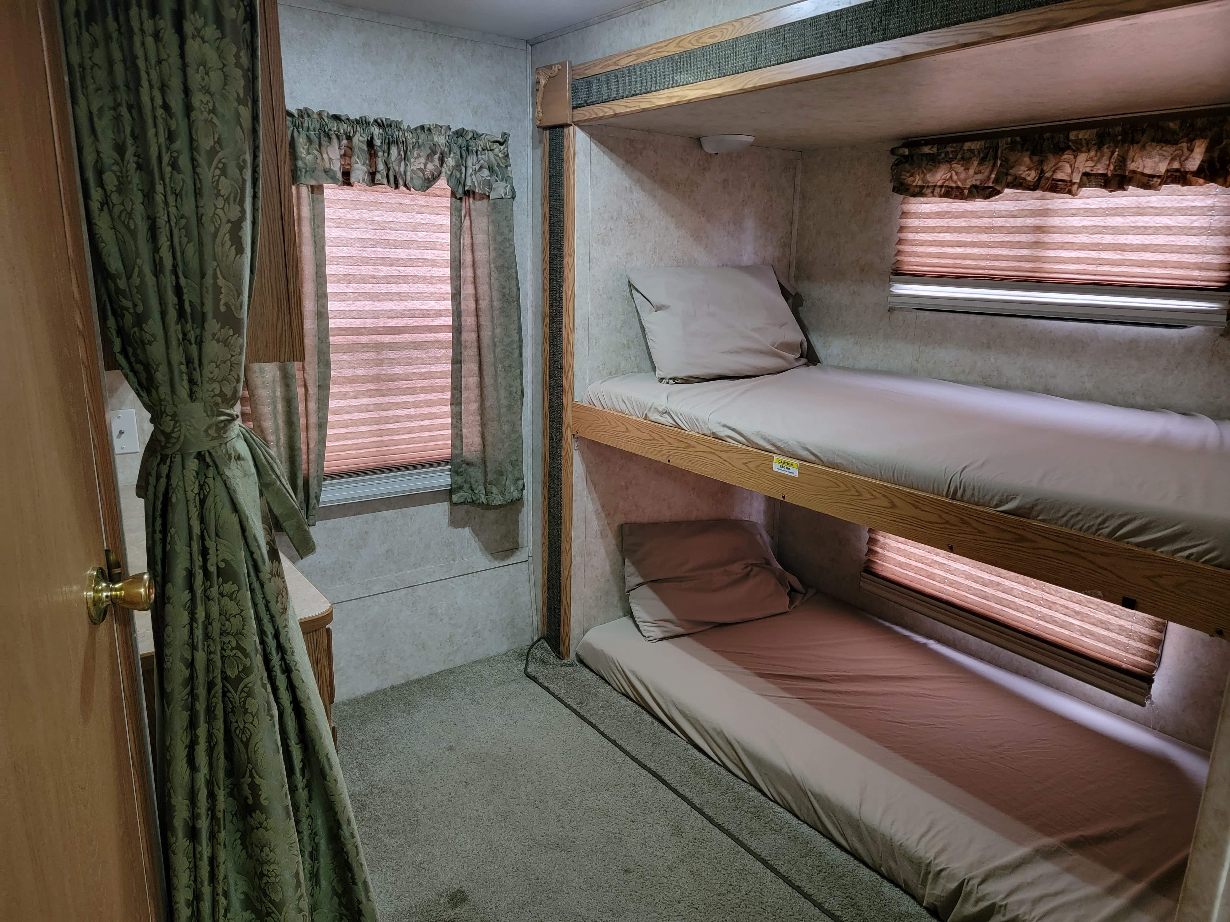 Cozy RV rental bunk beds with light bedding, window blinds, and patterned curtains, ideal for compact sleeping arrangements.. Keystone Cougar 2006