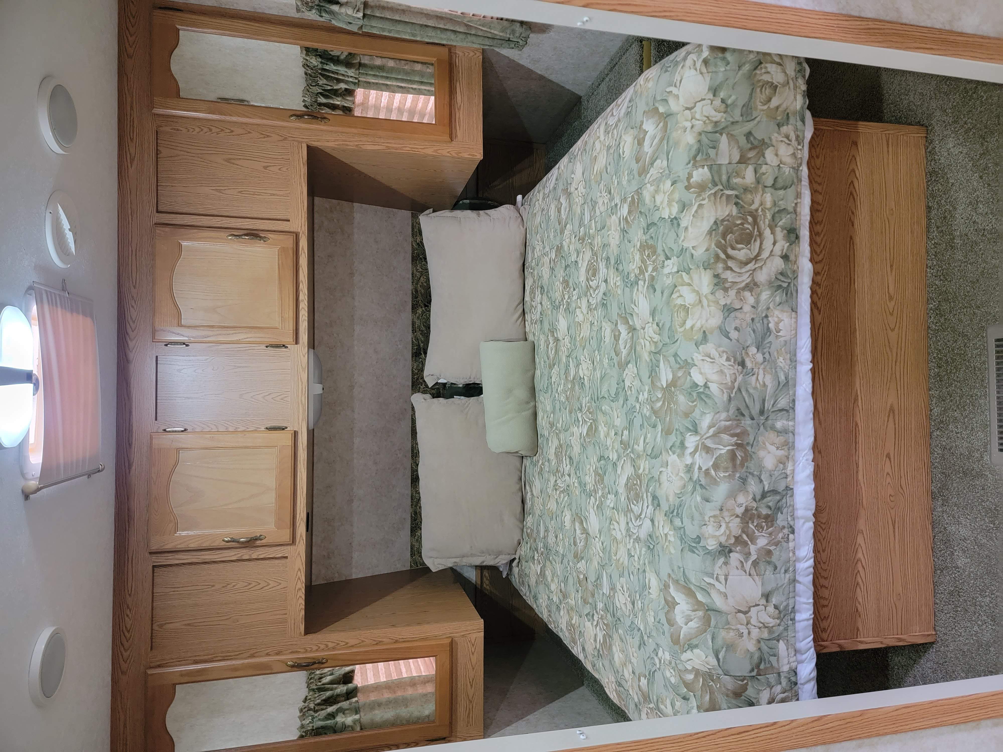 Cozy RV rental bedroom with floral bed, light wood cabinets, and integrated storage space.. Keystone Cougar 2006