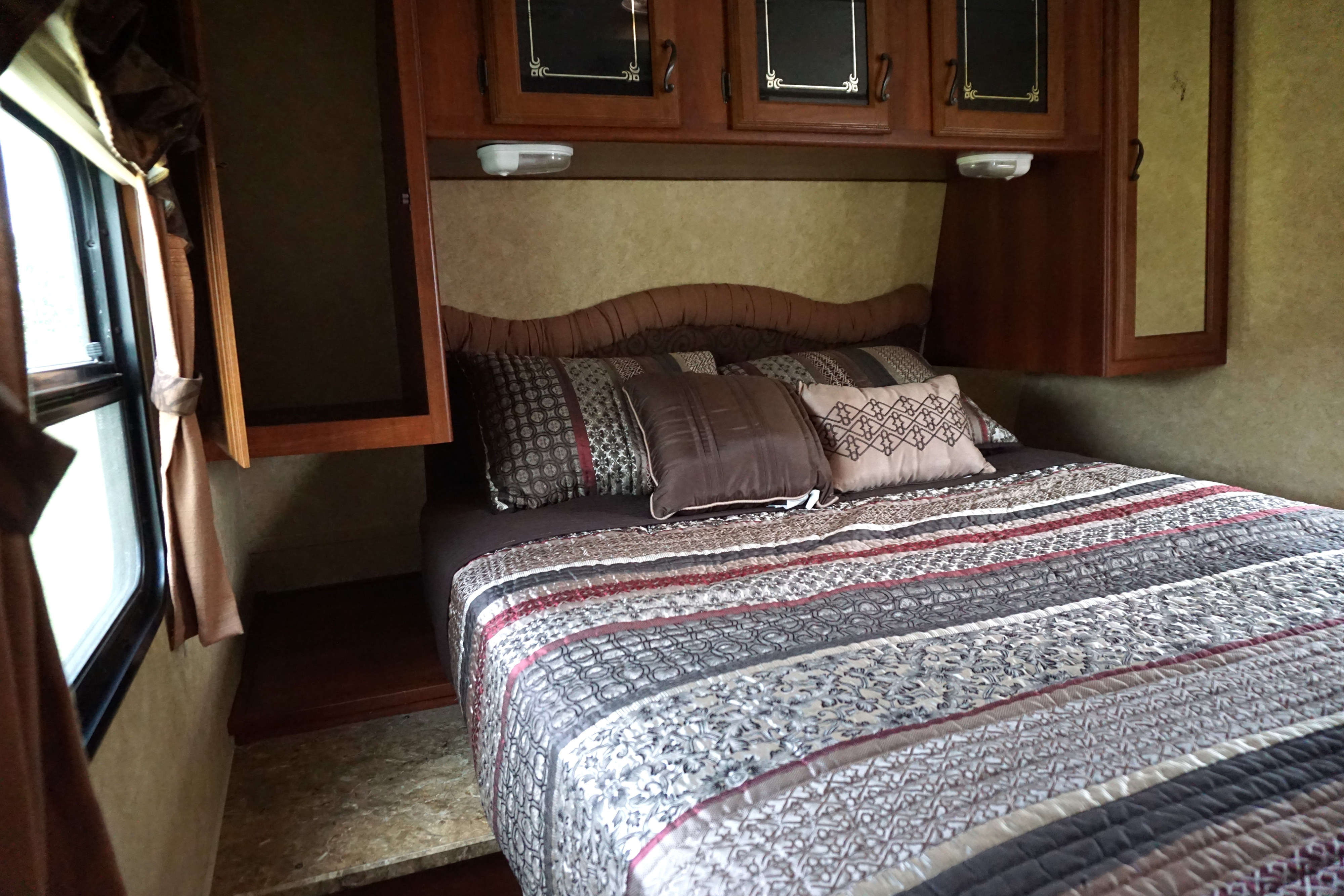 Cozy RV rental bedroom featuring a bed with patterned quilt, overhead cabinets, and a side window.. Forest River Tracer Executive 2011
