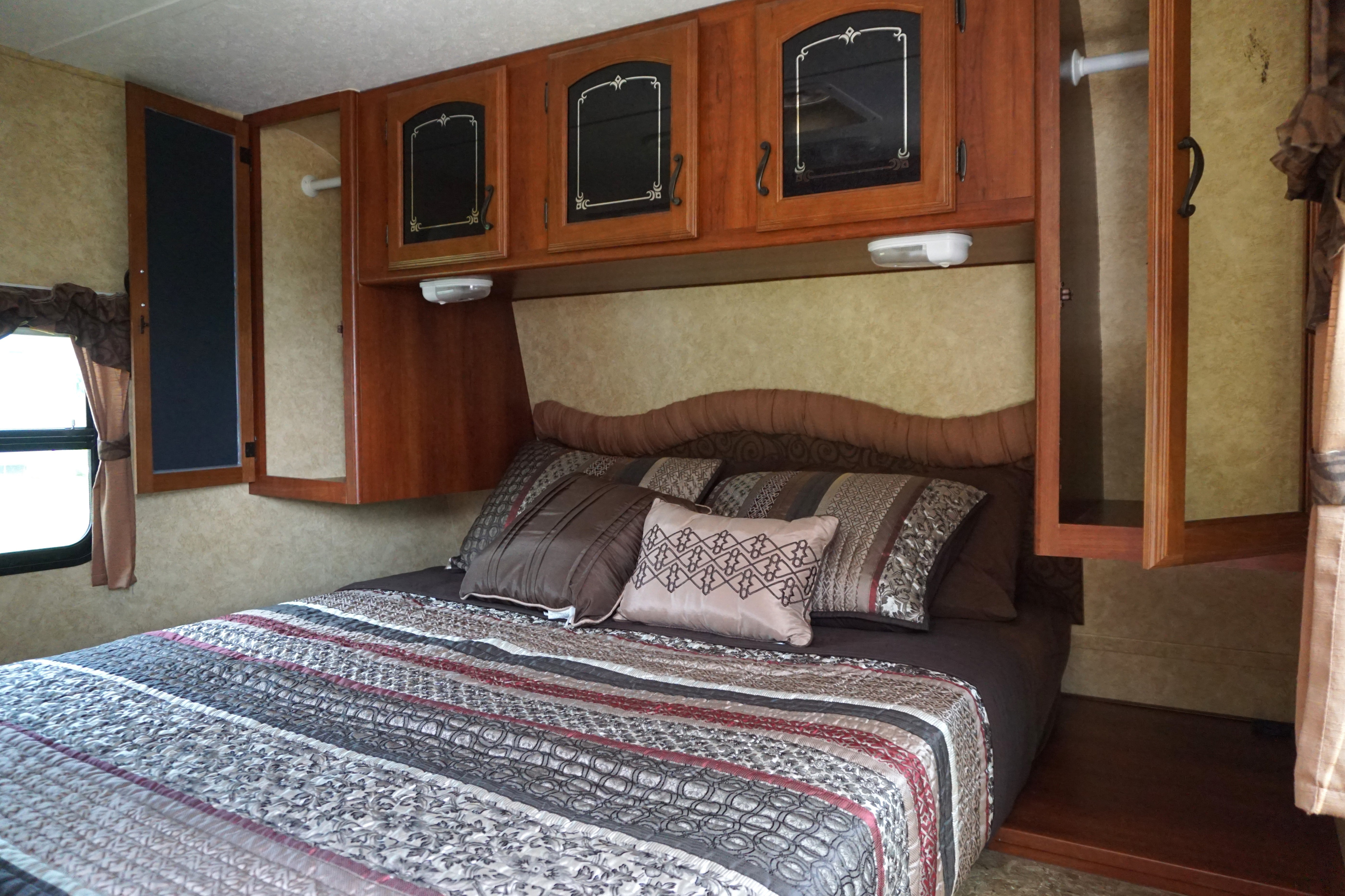Inside an RV rental: a cozy bedroom featuring a bed, ornate overhead cabinets, window, and wardrobe storage.. Forest River Tracer Executive 2011