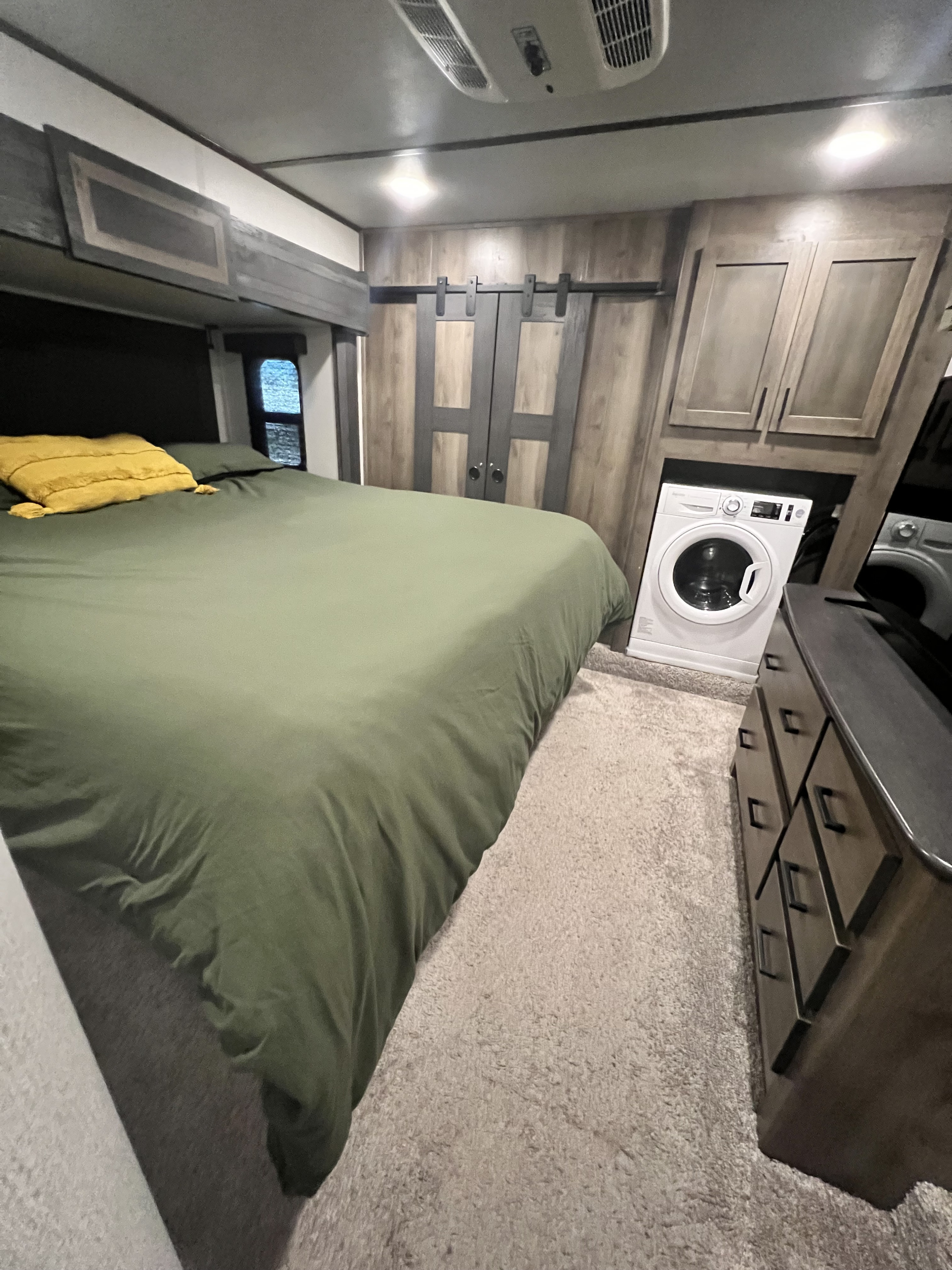 RV rental bedroom with green bed, compact washing machine, and wood cabinetry.. Keystone RV Sprinter Limited 2020
