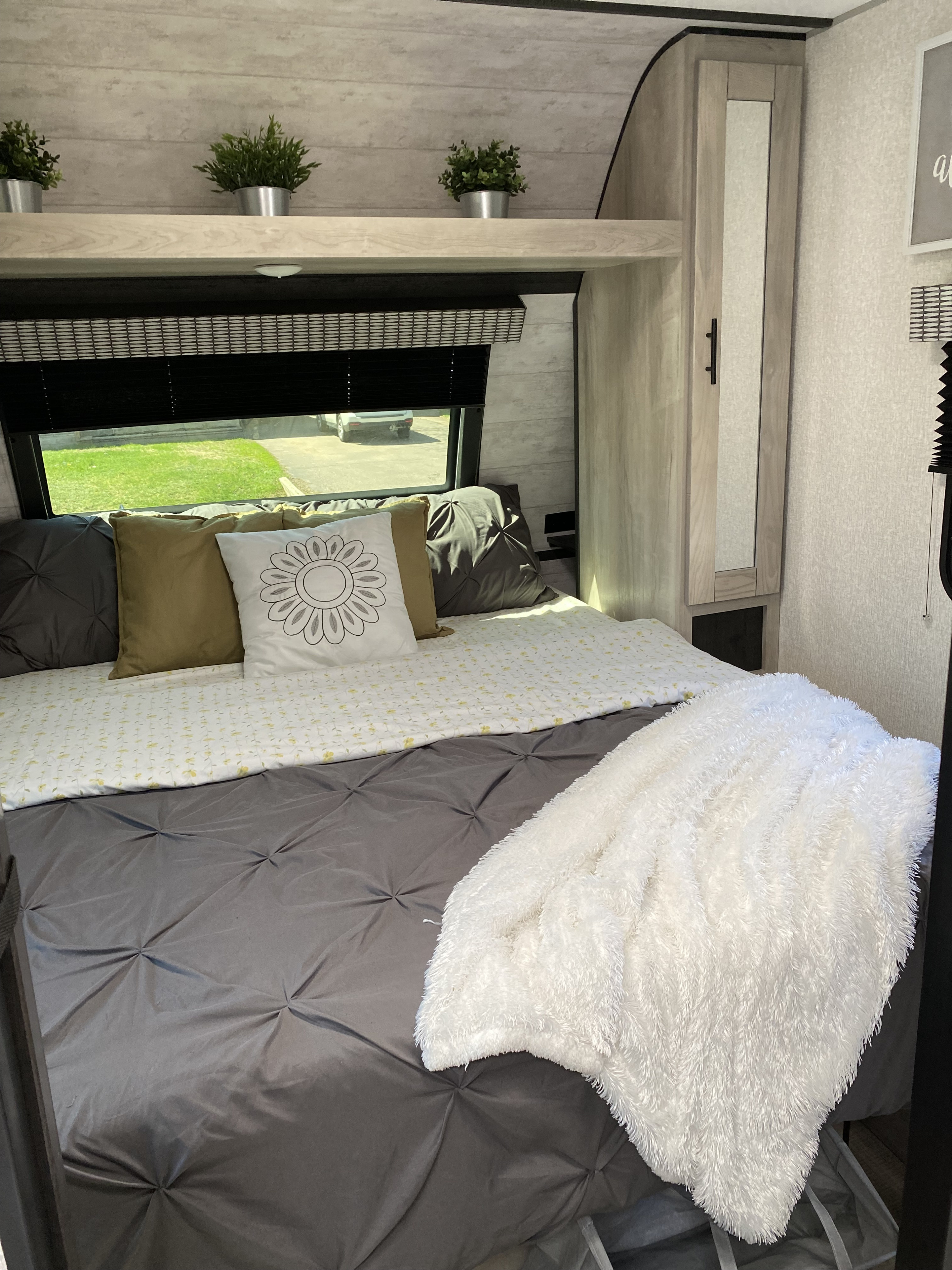 A cozy RV rental bedroom features a comfortable bed with a white fluffy blanket, overhead plants, and storage.. Connect Connect Trailer 2022