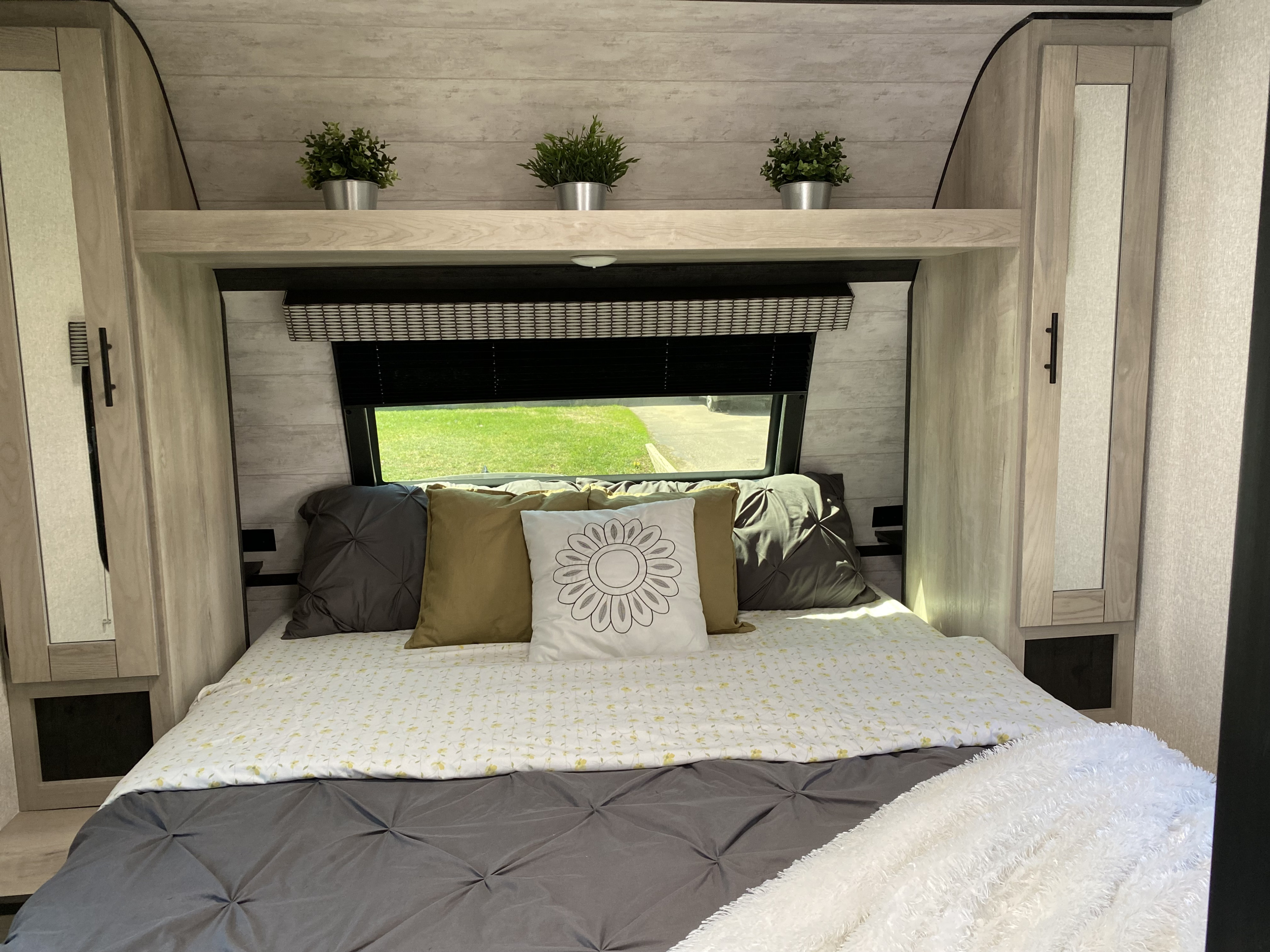 Cozy RV rental bedroom with a comfy bed, storage, and decorative plants on the overhead shelf.. Connect Connect Trailer 2022