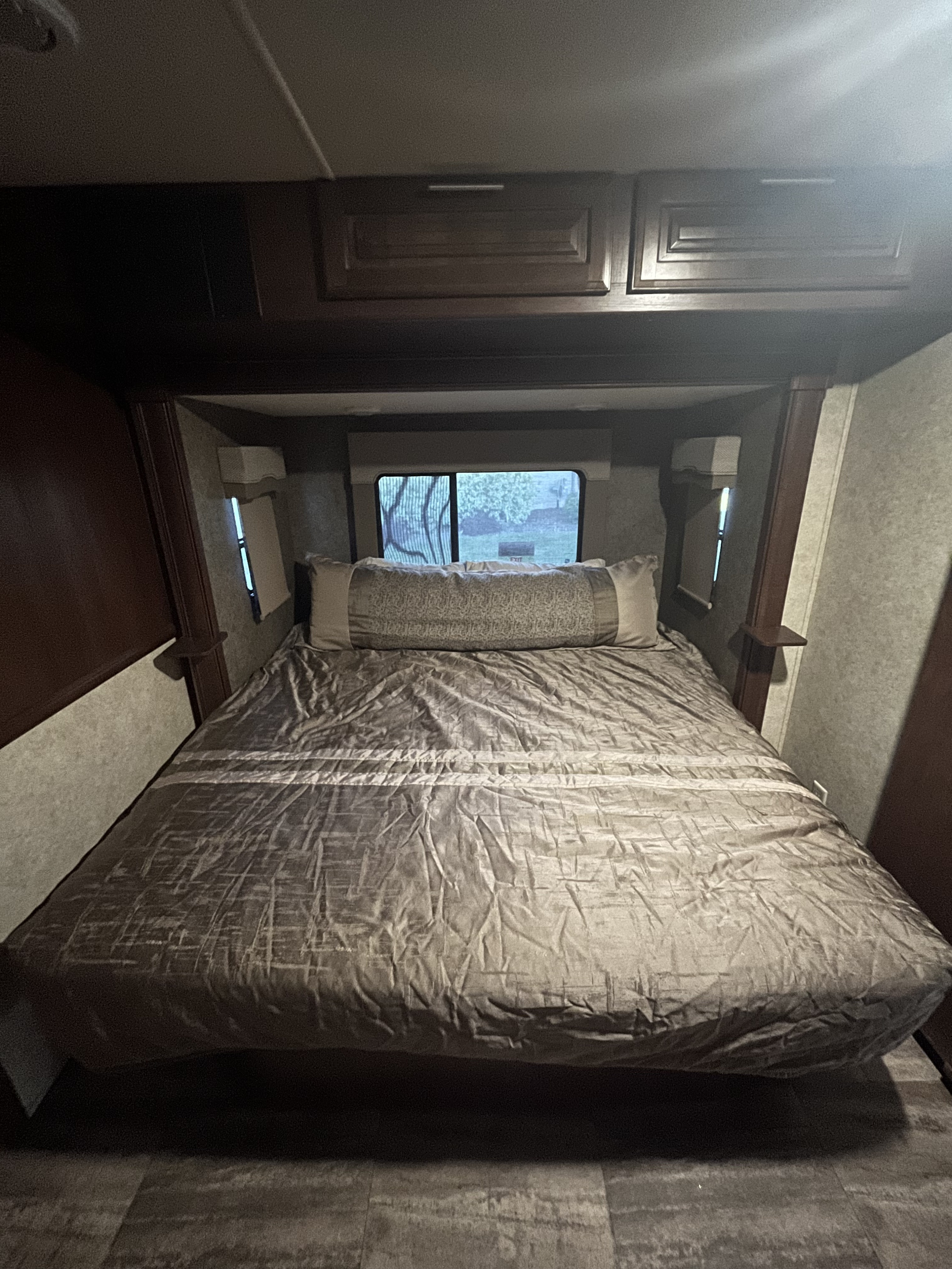 RV rental interior: A cozy bedroom with a bed, long pillow, overhead cabinets, and a window showing trees.. Georgetown 364TSF 2017