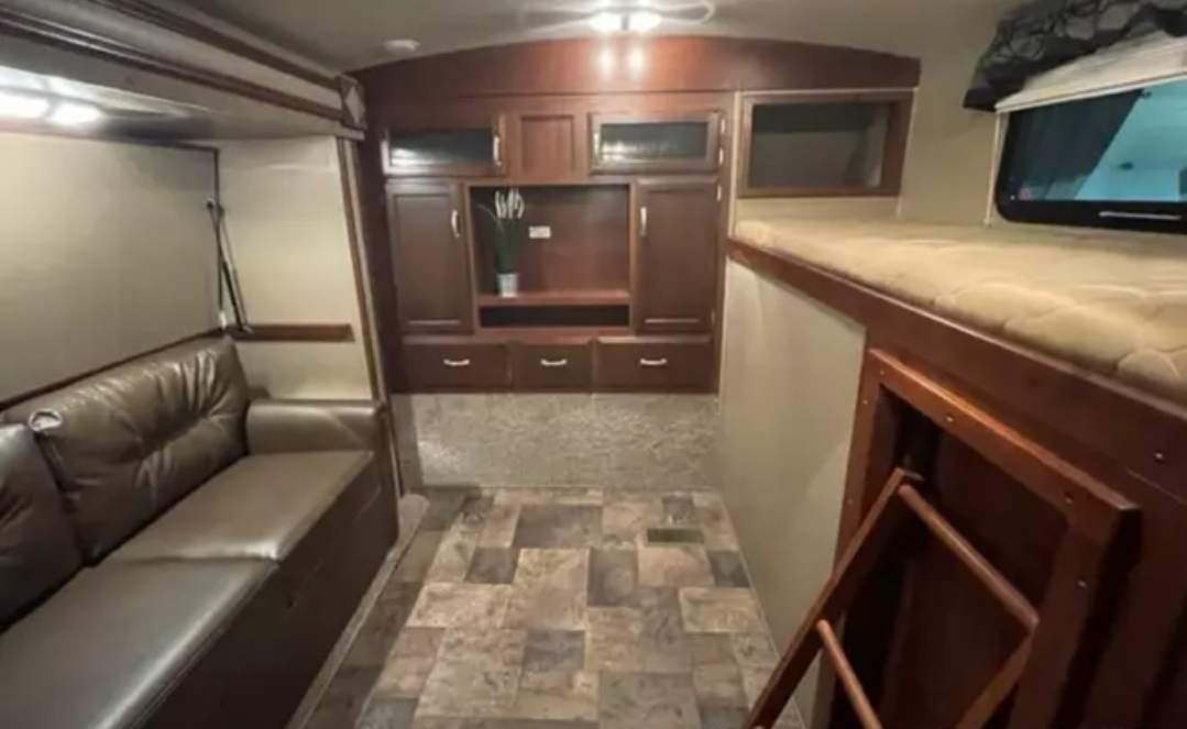 RV rental interior showcasing a brown sofa, central entertainment unit, and bunk beds with a ladder. Tiled floor.. Keystone RV Outback Terrain 2015