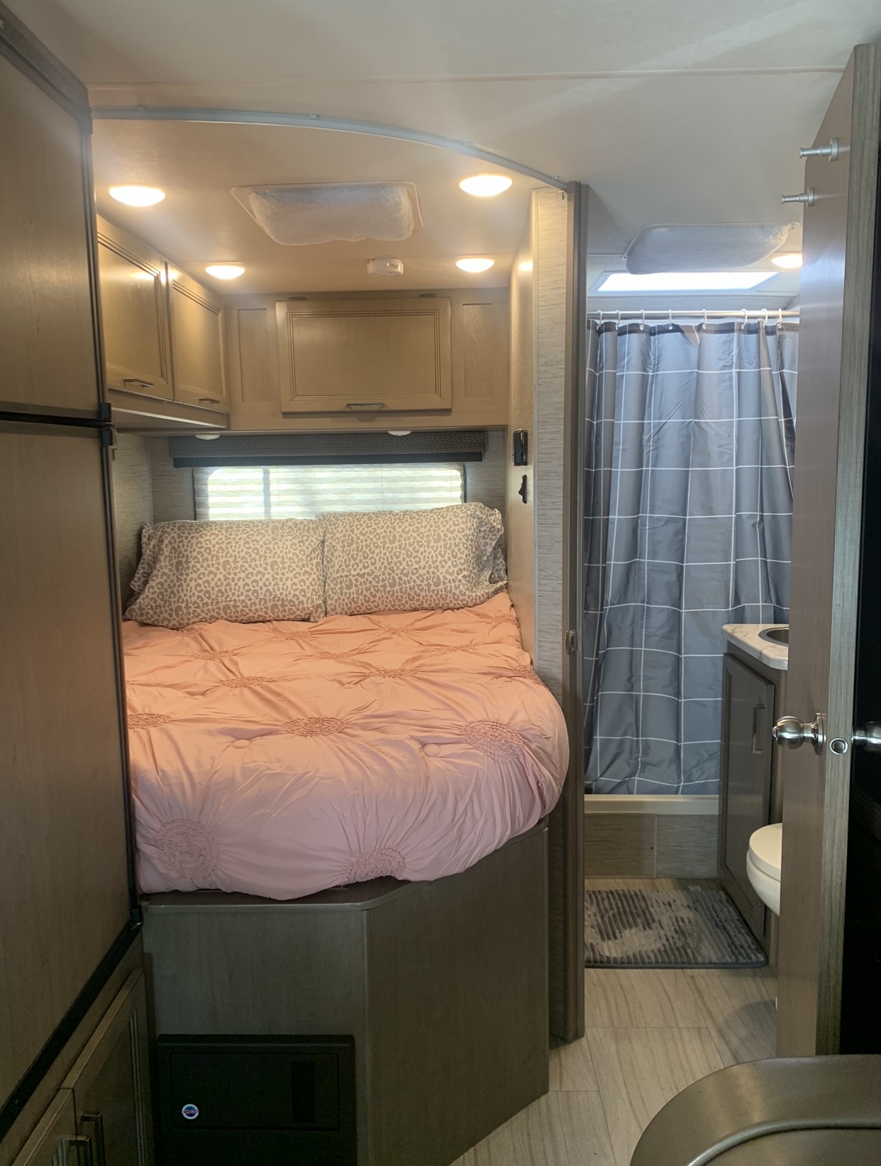 Cozy RV rental interior with a bedroom area (bed, patterned pillows, cabinets) and compact bathroom (shower, vanity).. Thor Motor Coach coleman 2021