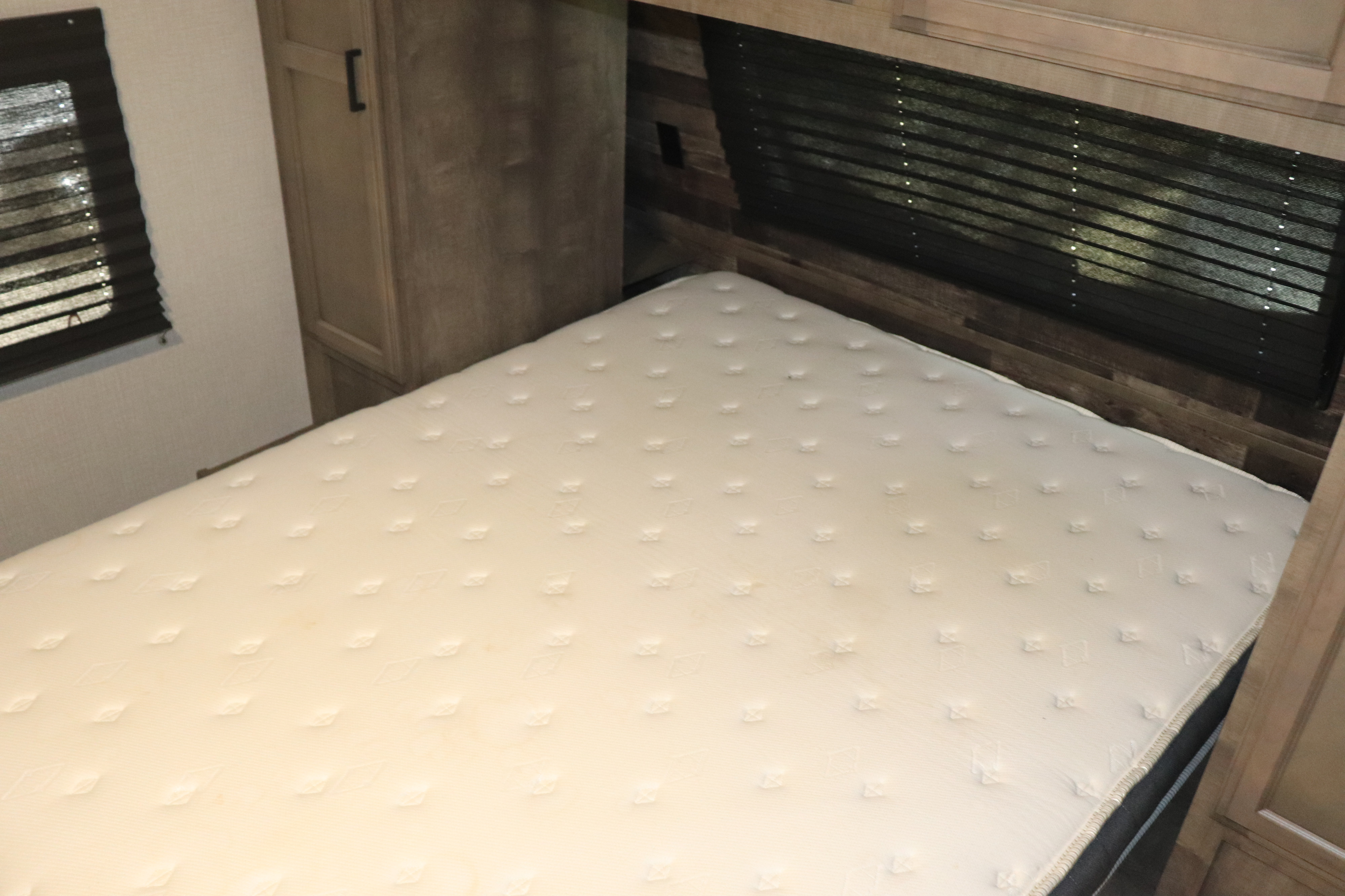 An RV rental bedroom with a clean white mattress, framed by dark blinds on the windows and light wood cabinets.. Venture Rv Sporttrek 2022