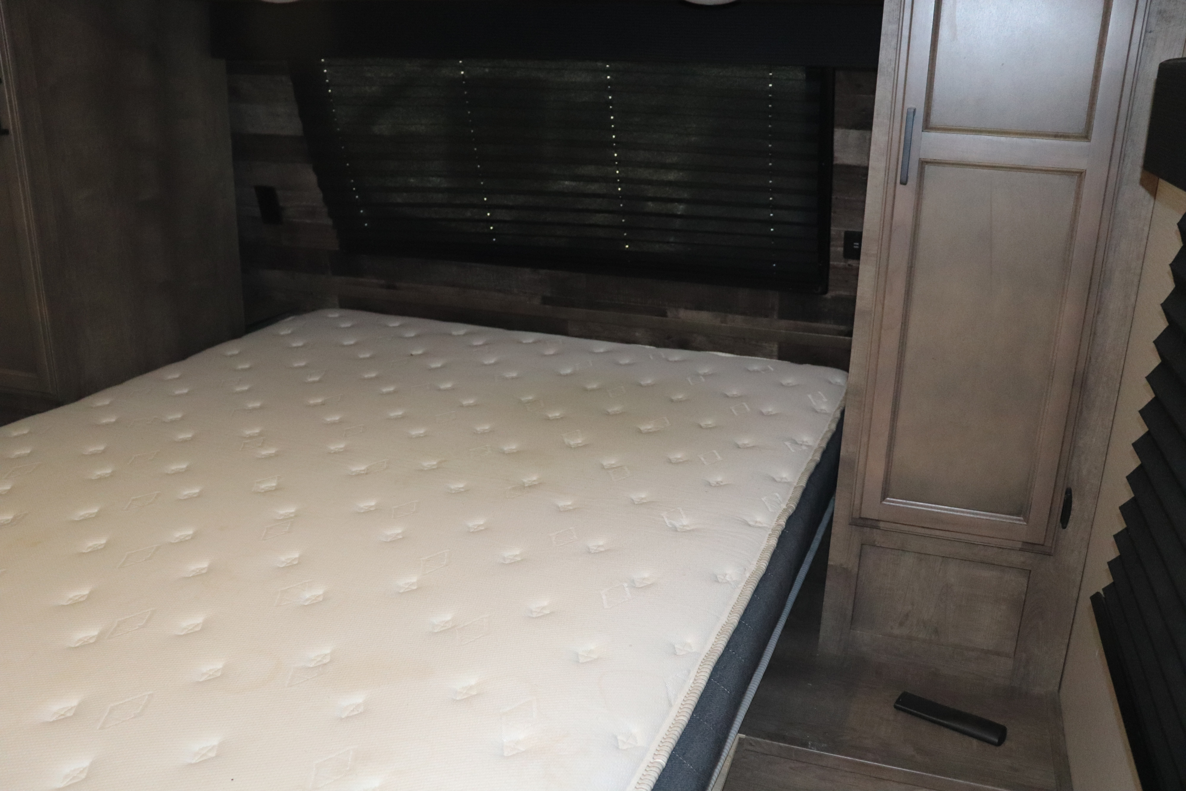RV rental bedroom showcasing a comfortable white mattress, dark window blinds, and wood-toned built-in cabinetry.. Venture Rv Sporttrek 2022