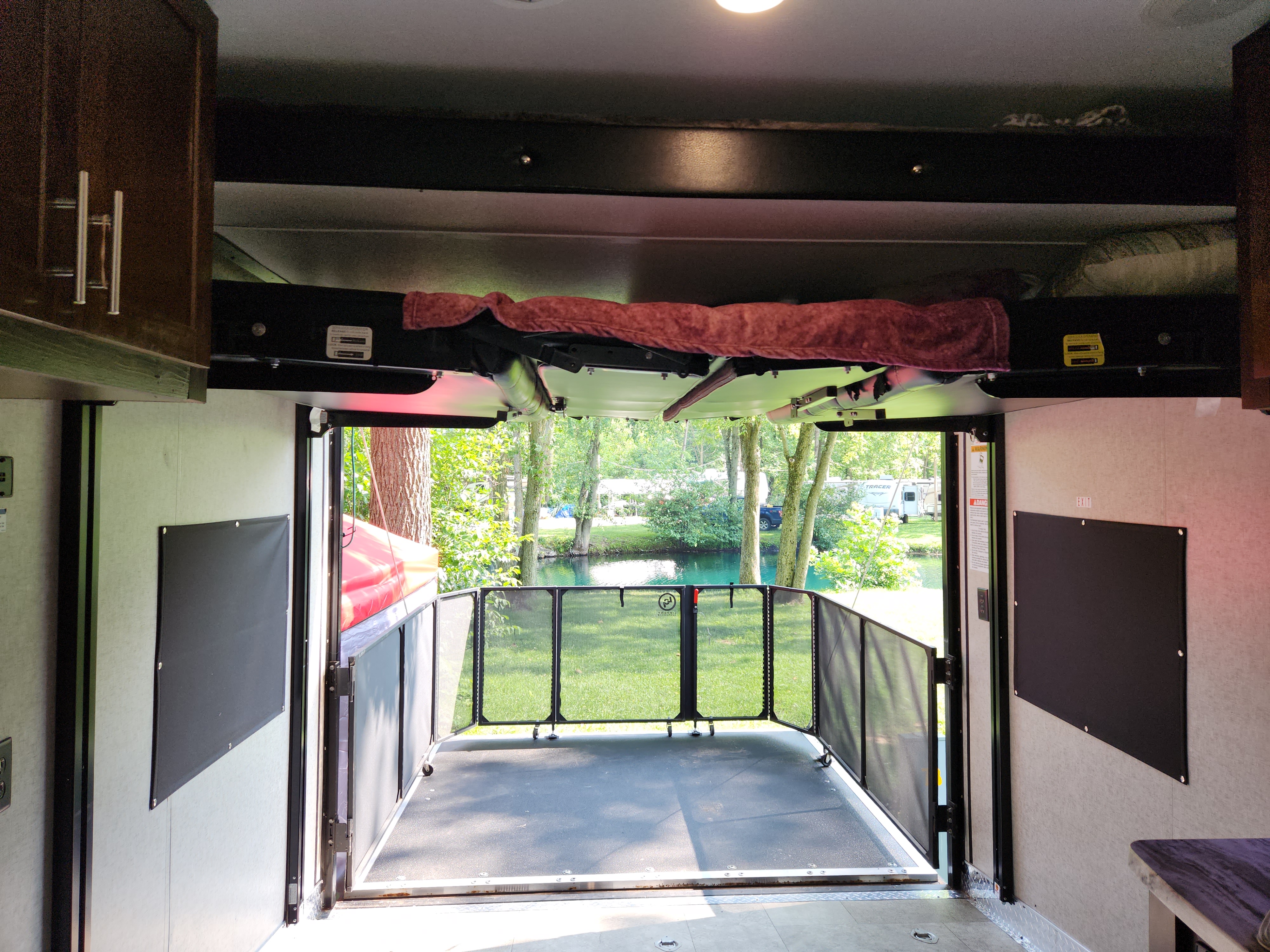 RV rental toy hauler with deck open to a tranquil campground, showing a water view & trees. Ideal for outdoor living.. Forest River Vengeance 2019