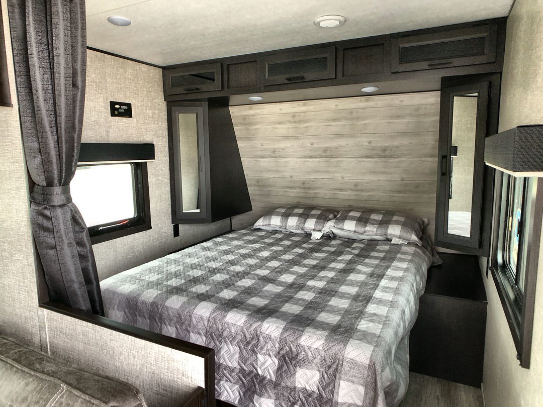 Cozy RV rental bedroom showing a bed with checkered quilt, overhead cabinets, and curtained windows. Perfect for travel.. Jayco Jay Flight 2022