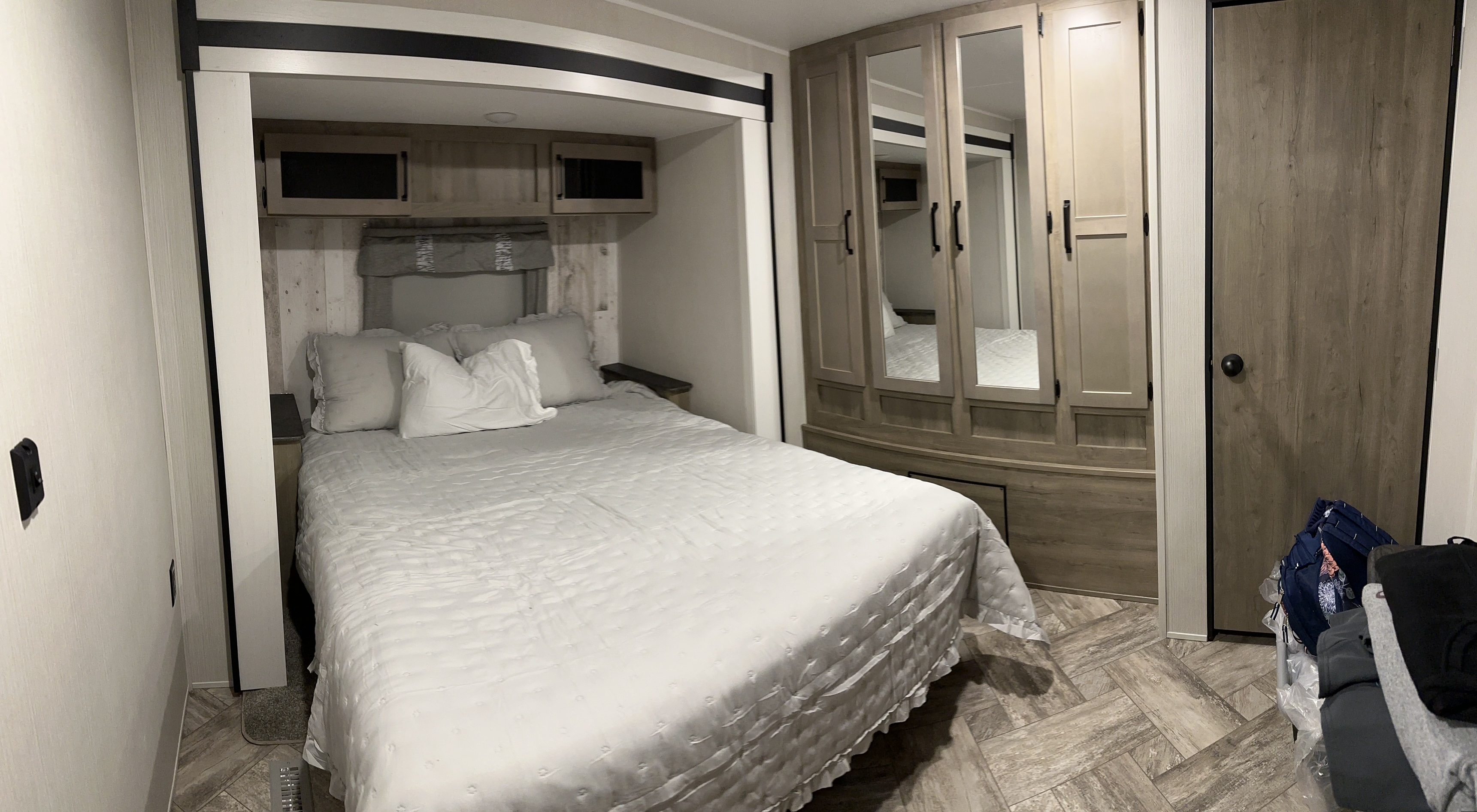 RV rental bedroom showcasing a comfortable bed, overhead cabinets, large mirrored wardrobe, and wood-look flooring.. Forest River Palomino Puma 2023