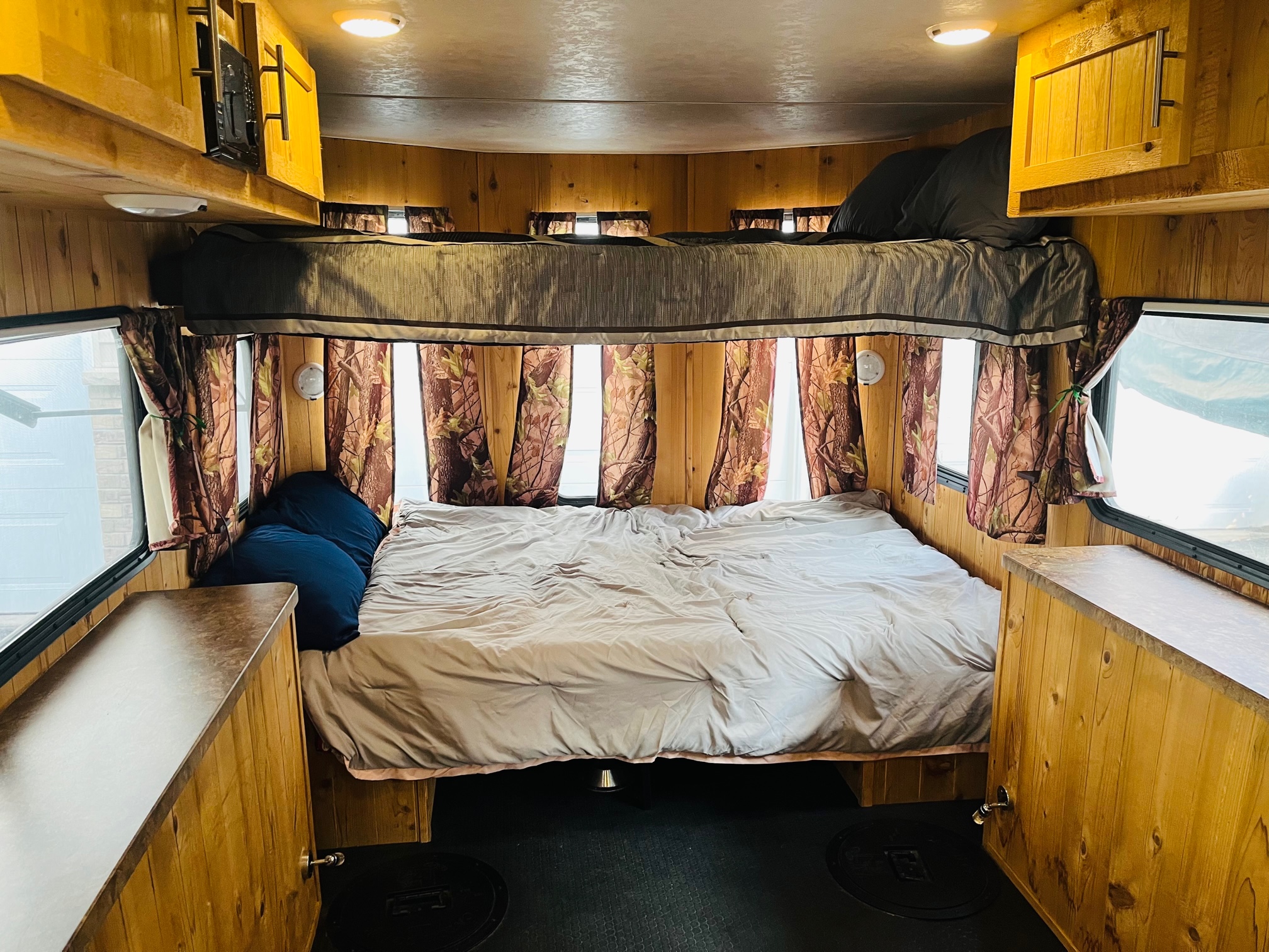 Spacious RV rental interior featuring a main lower bed, upper bunk, wooden paneling, and practical side storage.. Forest River Cherokee Grey Wolf 2015