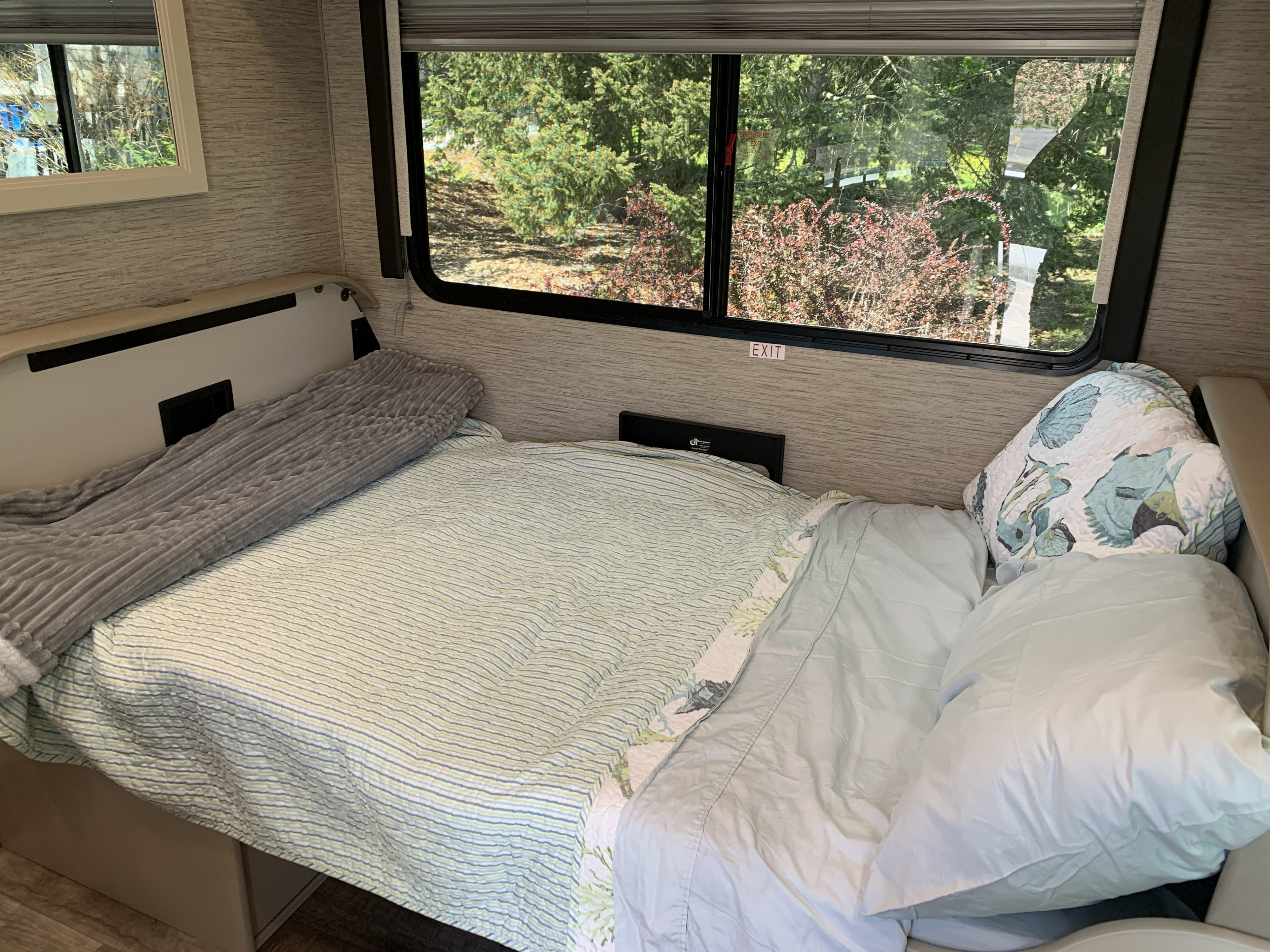 Cozy RV rental bedroom with window view of nature. Bed made, ready for a comfortable stay.. Thor Chateau 2023