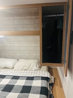 RV rental bedroom featuring a comfortable bed with checkered blanket and an open, compact wardrobe.. Forest River Prime Time Avenger 24BHSLE 2023