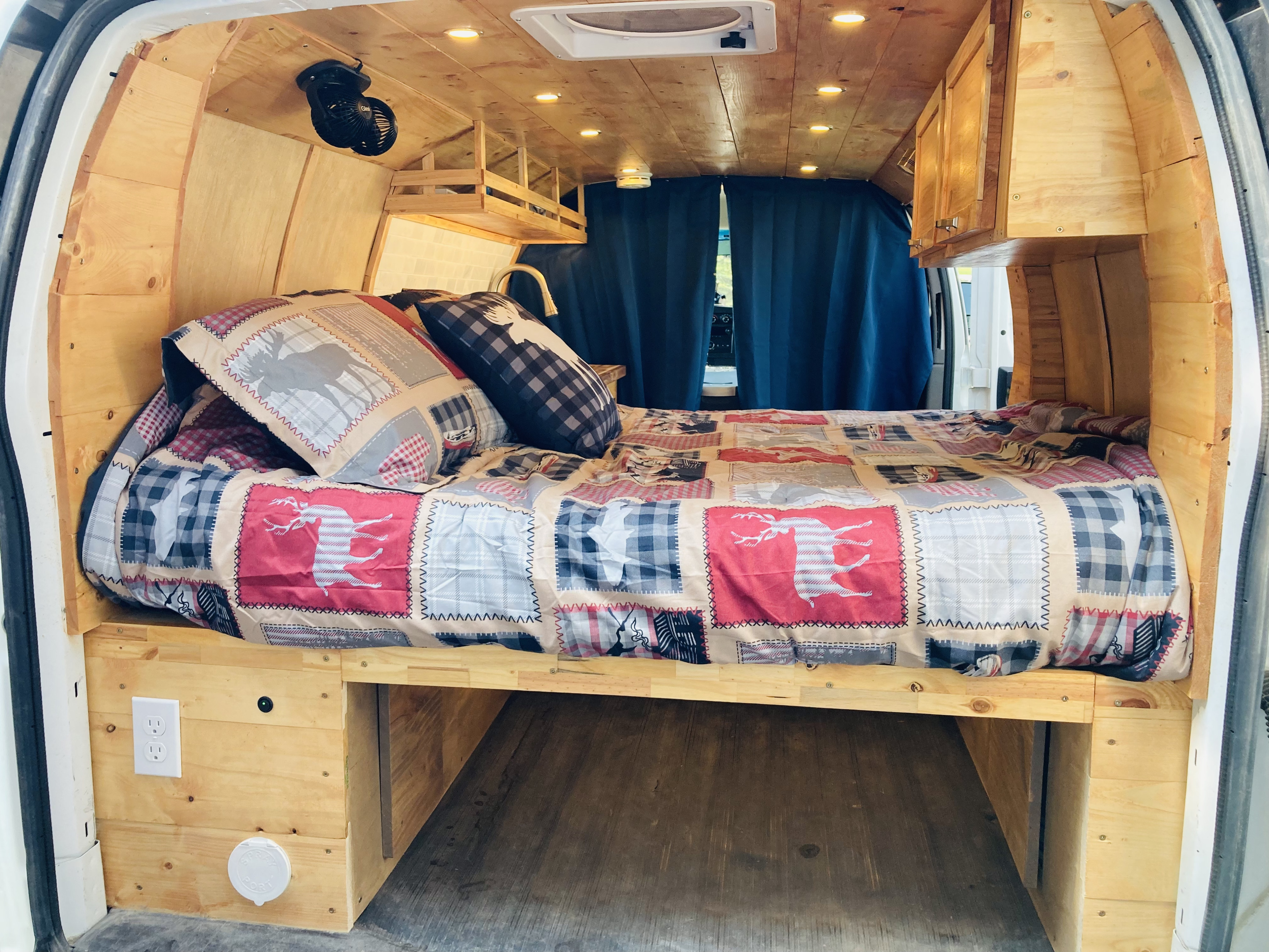 Explore this cozy RV rental interior featuring wooden paneling, a large bed with patterned bedding, and practical features.. Ford Econoline 2012